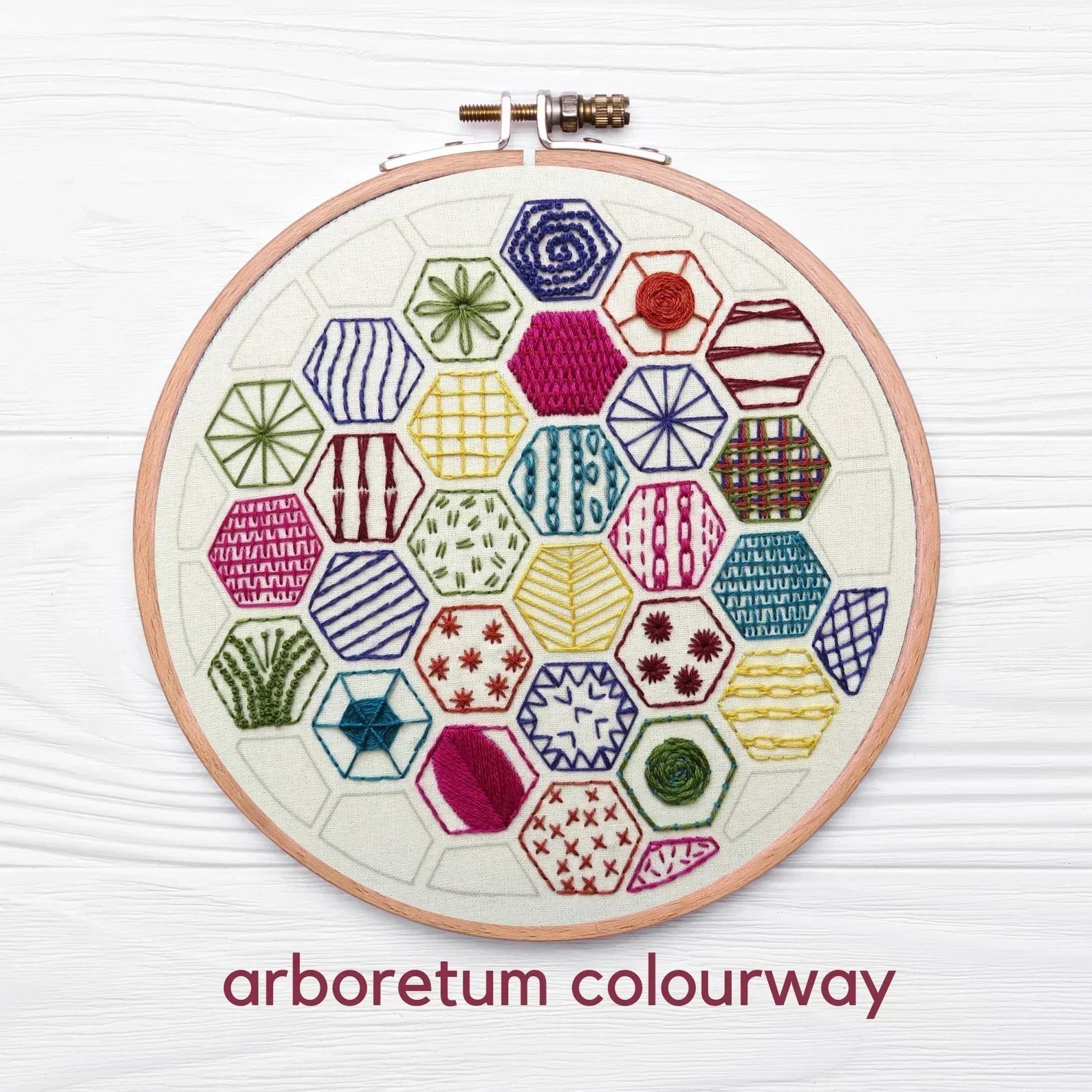 Embroidery hoop with colorful geometric patterns on a white background, labeled 'arboretum colourway'.