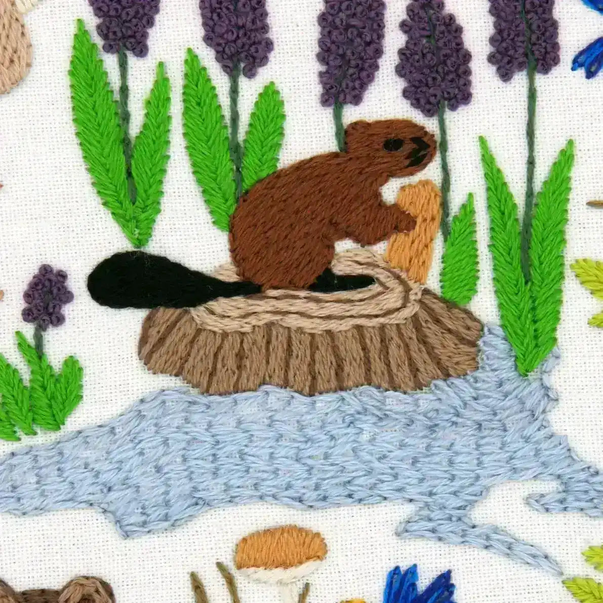 Embroidered design of a beaver on a log with plants and mushrooms