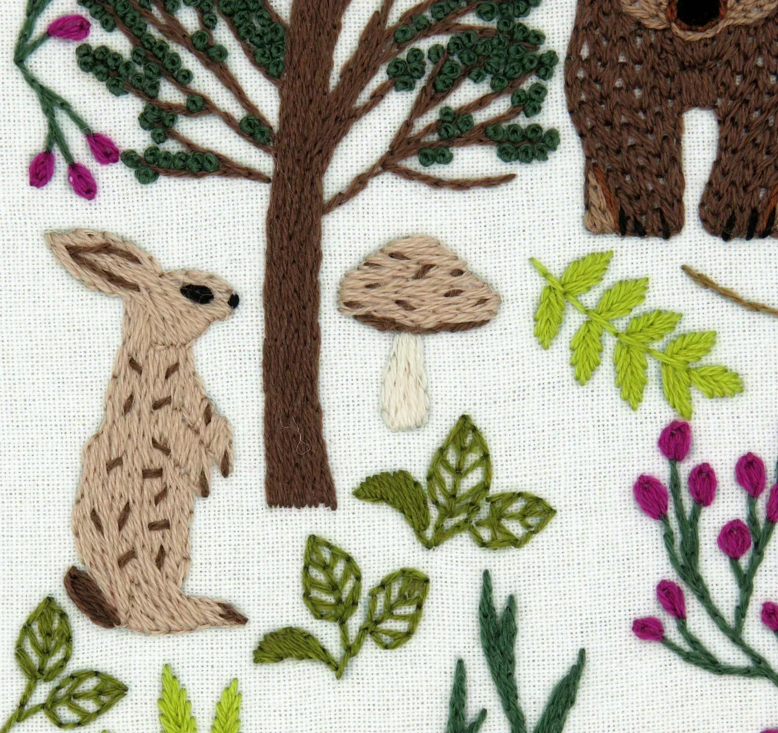 Embroidered design of a rabbit, tree, mushrooms, and plants on fabric.