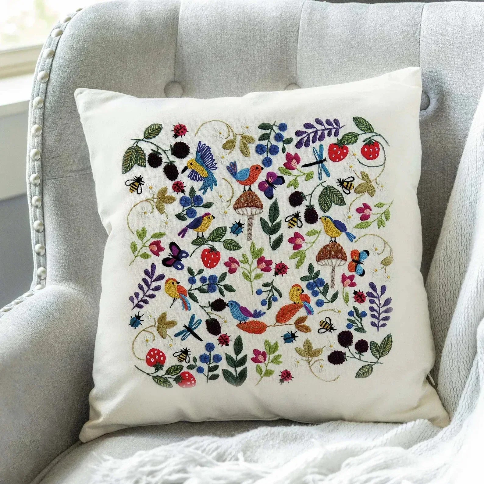 Decorative pillow with colorful floral and bird pattern on a gray chair.