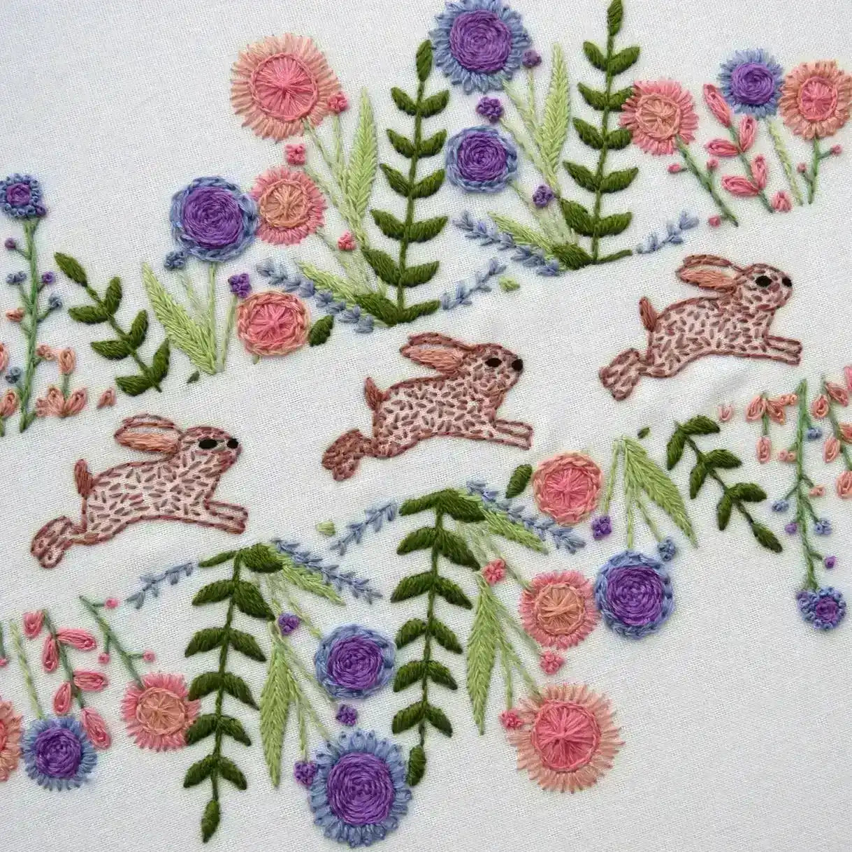 Embroidery design with rabbits and flowers on a white background
