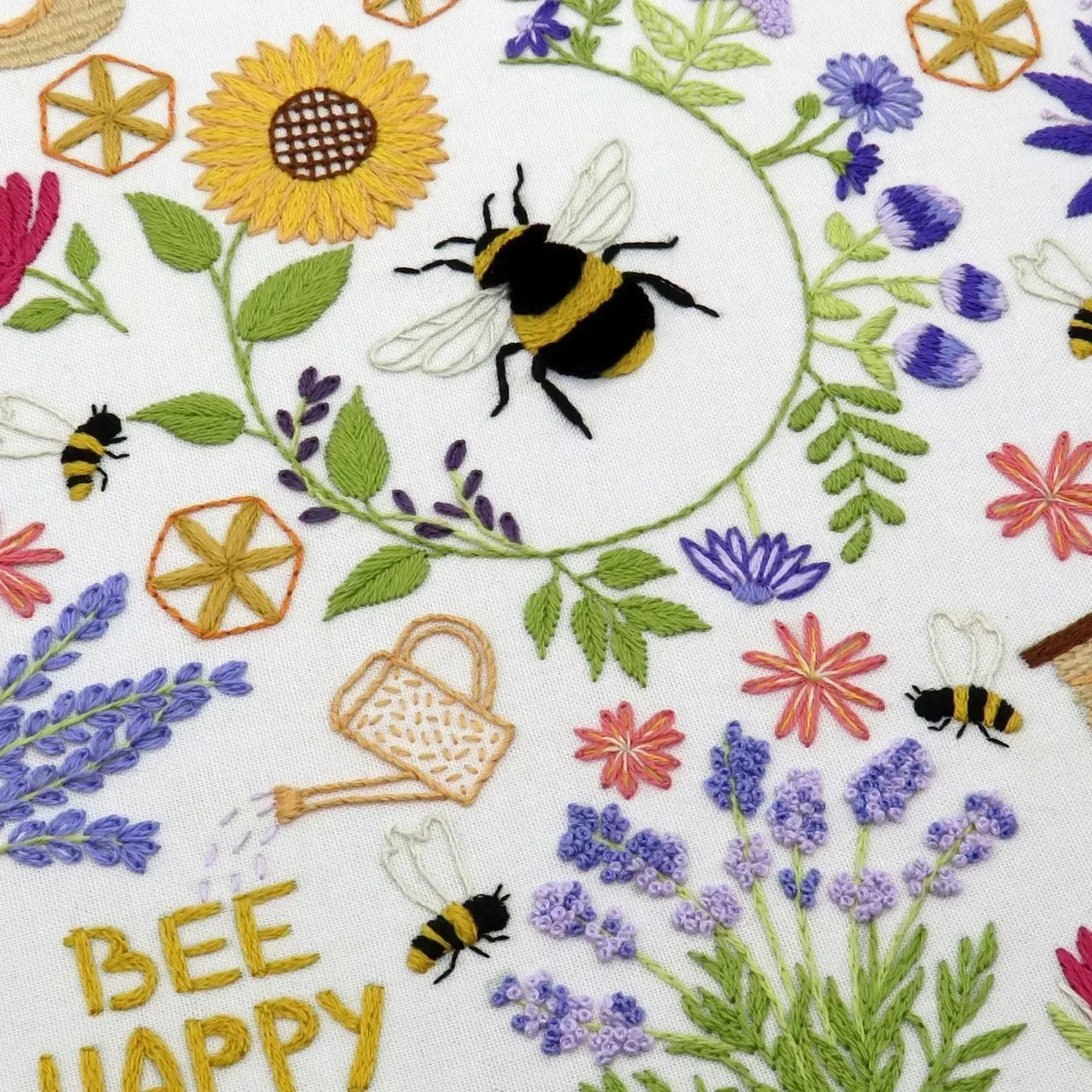 Embroidered design with bees, flowers, and the phrase 'Bee Happy' on a white background.
