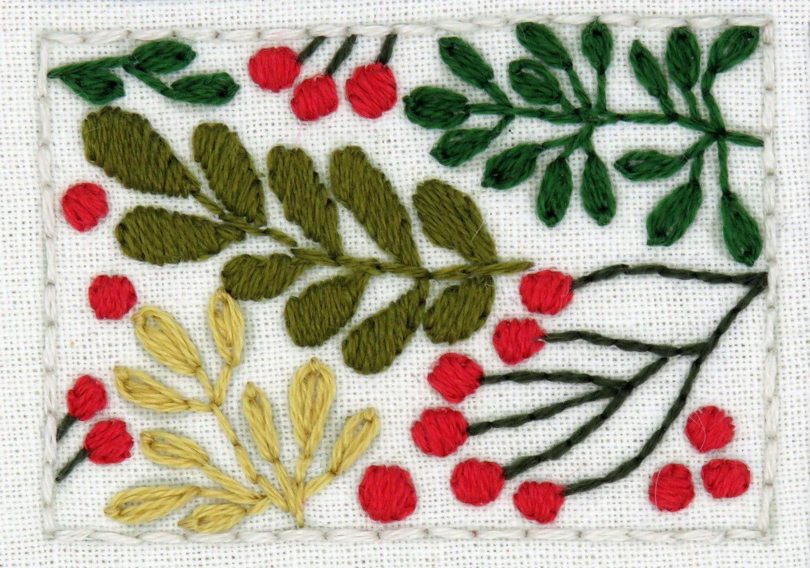 Embroidered design with green leaves, red berries, and yellow flowers on a white background