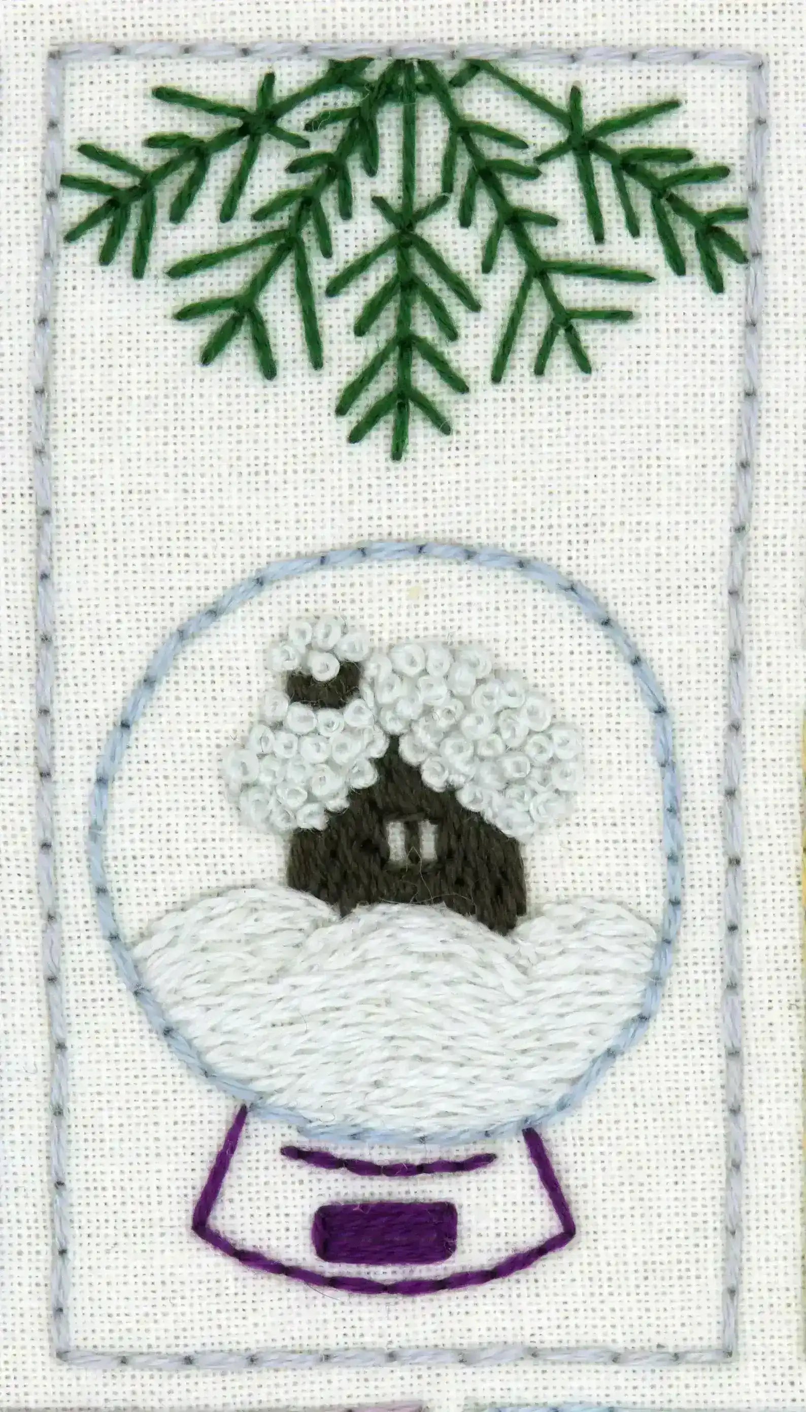 Embroidered design of a snow globe with a house and trees on a white background