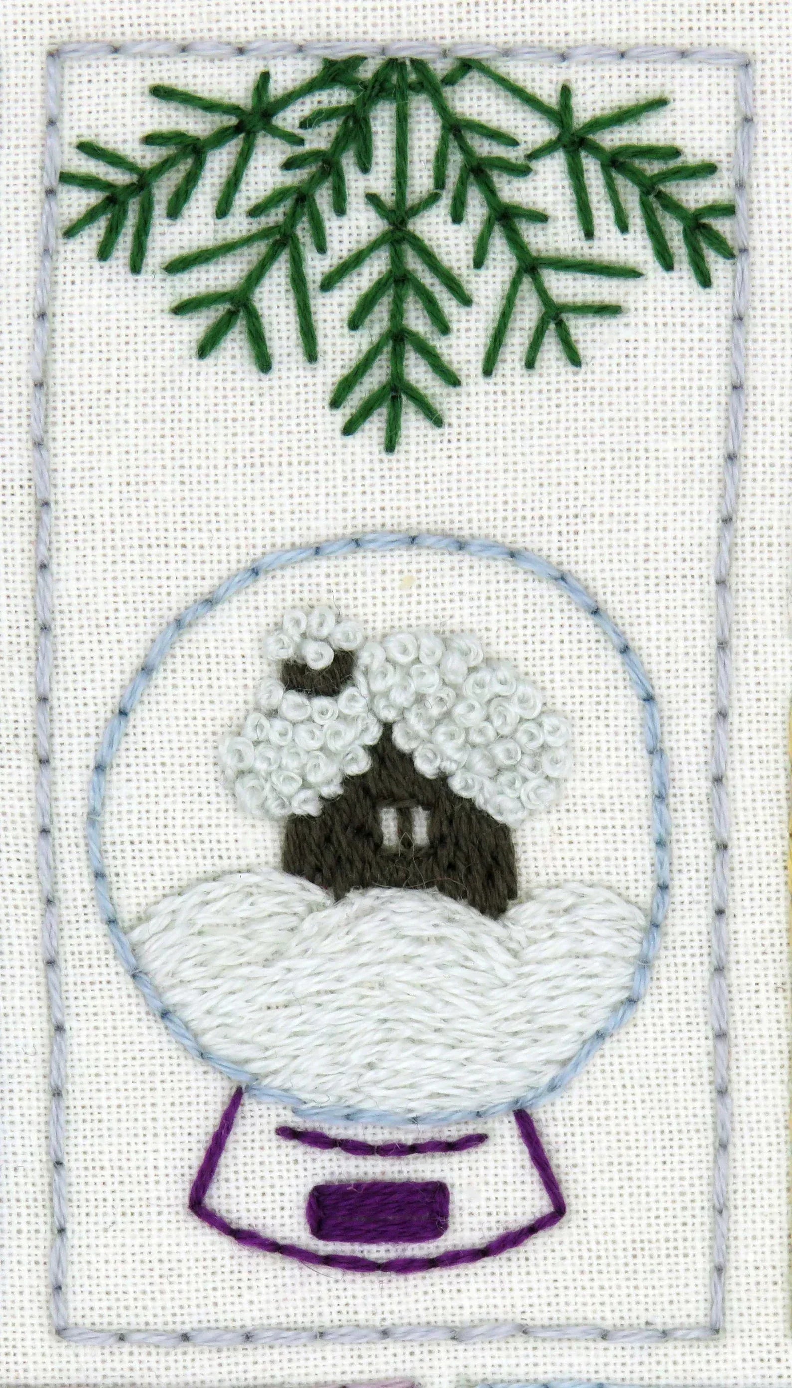 Embroidered design of a snow globe with a house and trees on a white background