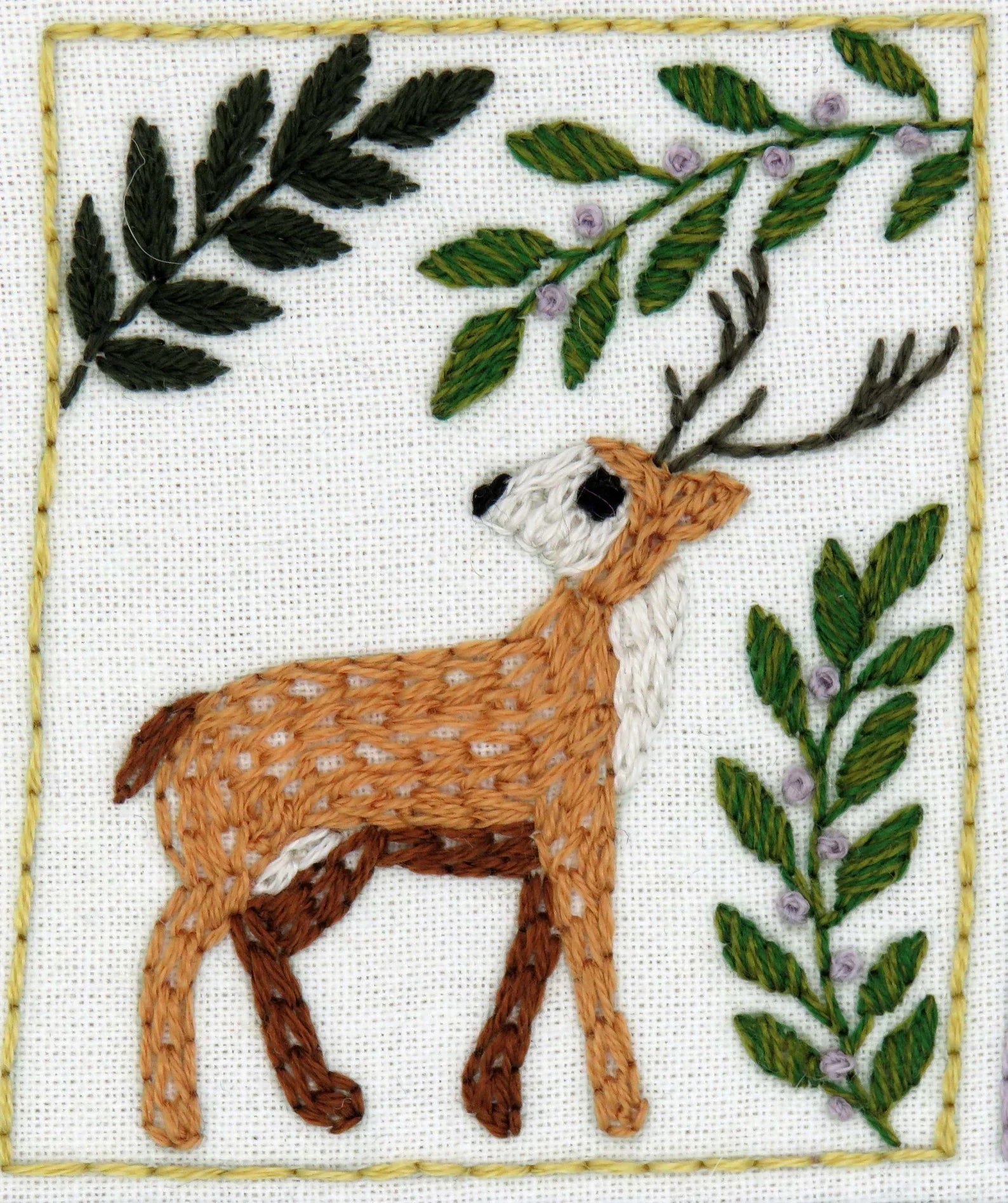 Embroidered design of a deer with leaves and flowers on a white background