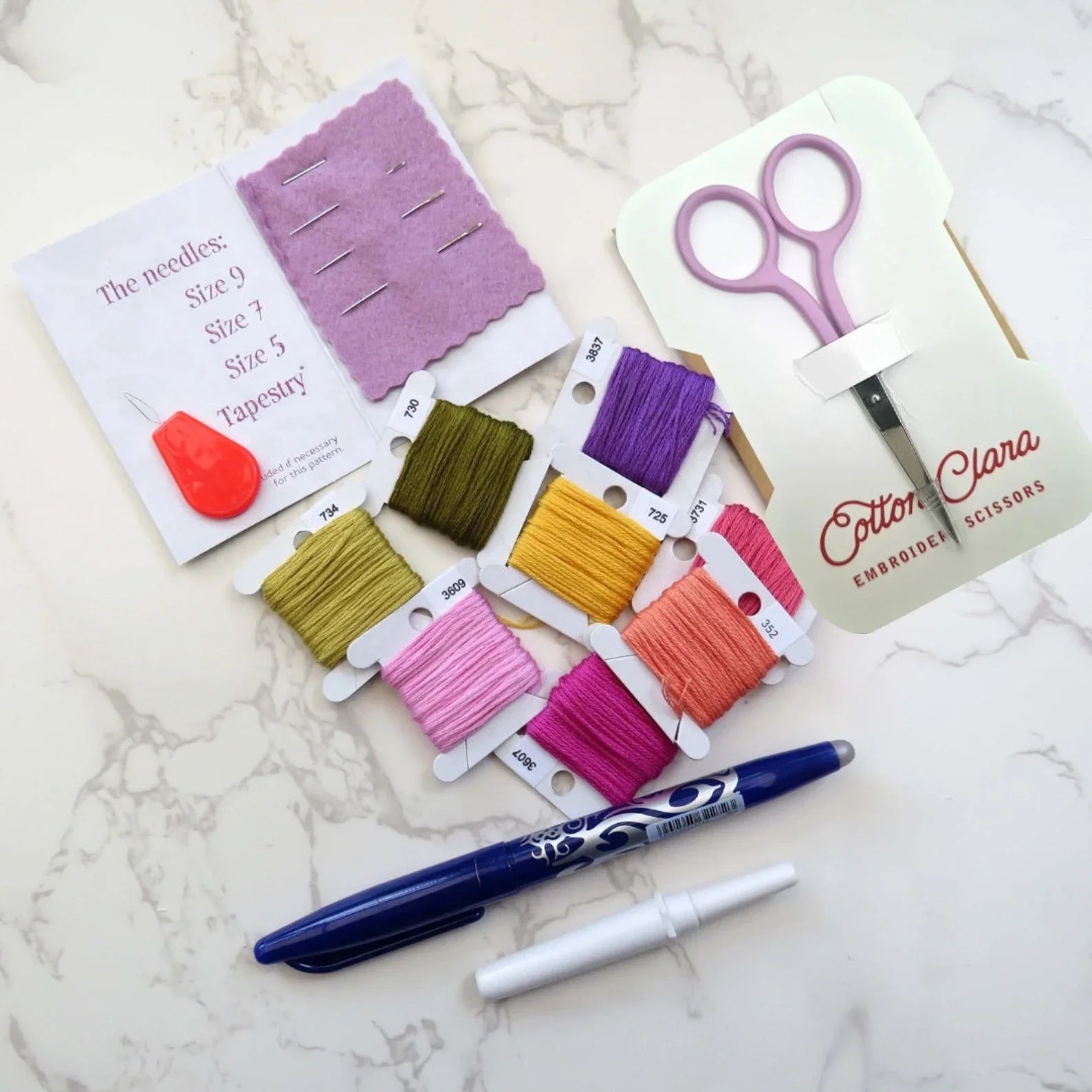 Sewing kit with colorful threads, scissors, and a pen on a marble surface