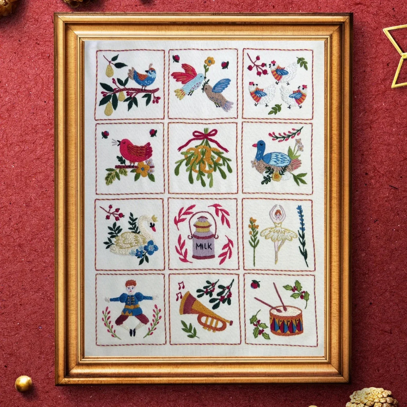 Framed cross-stitched sampler with various designs on a red background