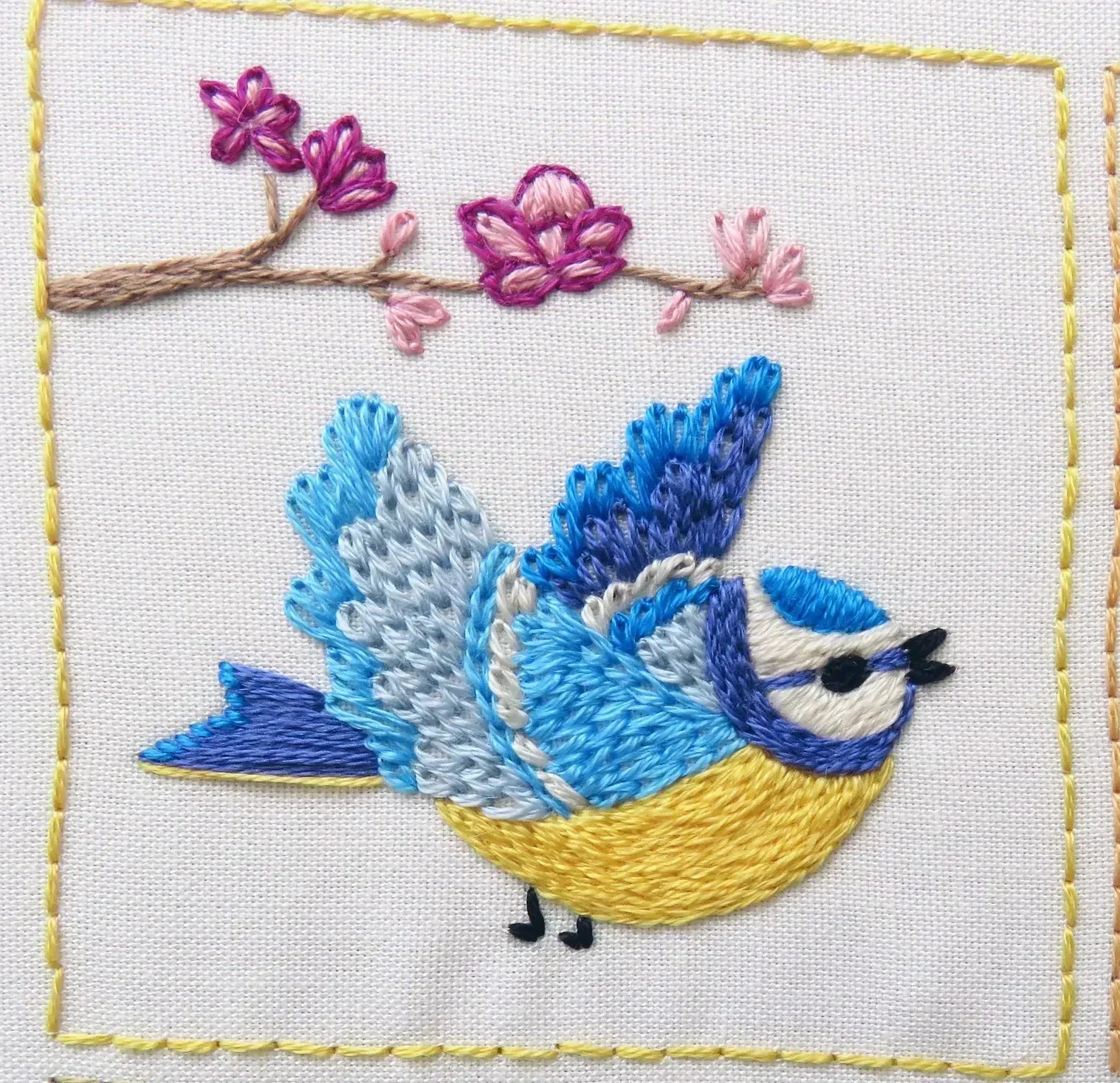 Embroidered design of a blue bird with pink flowers on a white background