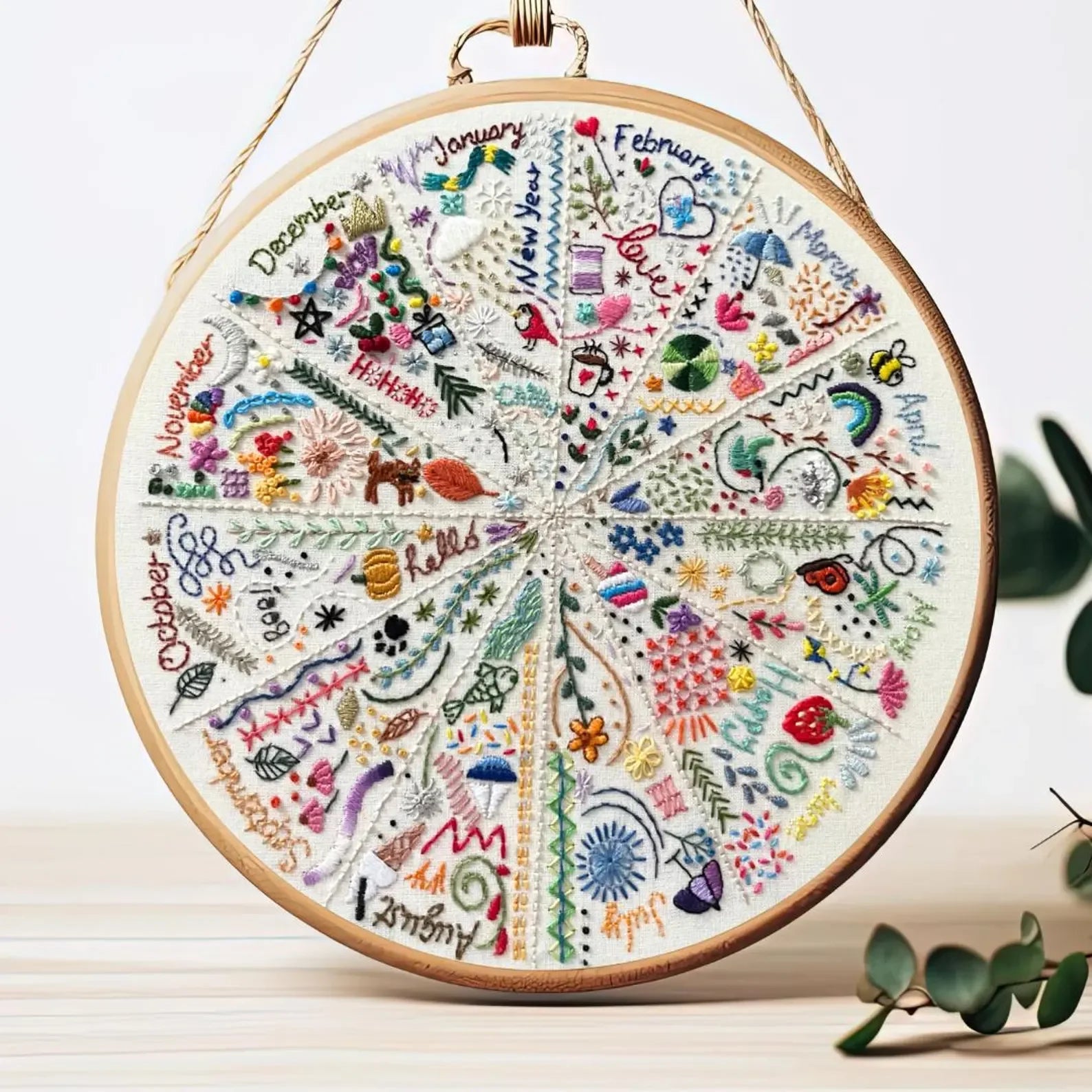 Embroidered circular design with months of the year on a wooden hoop.