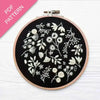 Embroidery hoop with white floral patterns on black fabric, pink PDF pattern label.