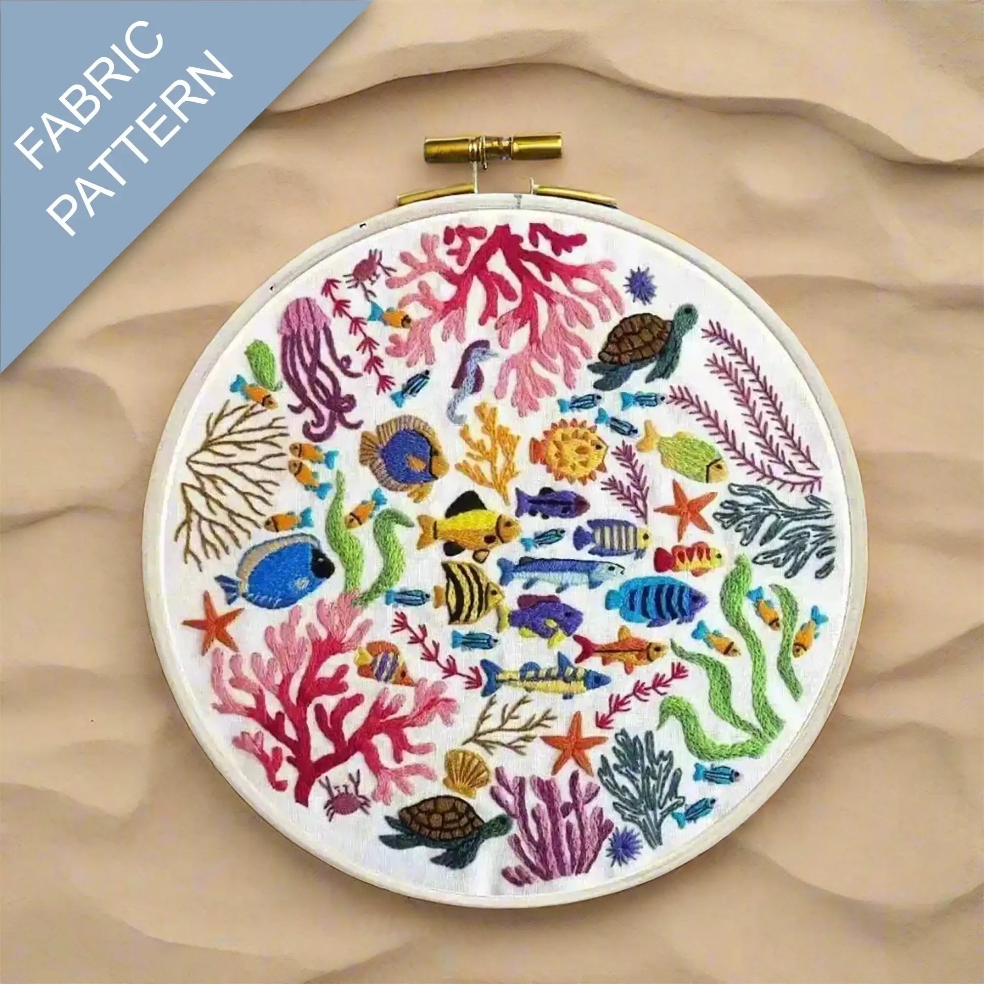 Embroidery hoop with colorful underwater scene including fish and coral on a fabric background.