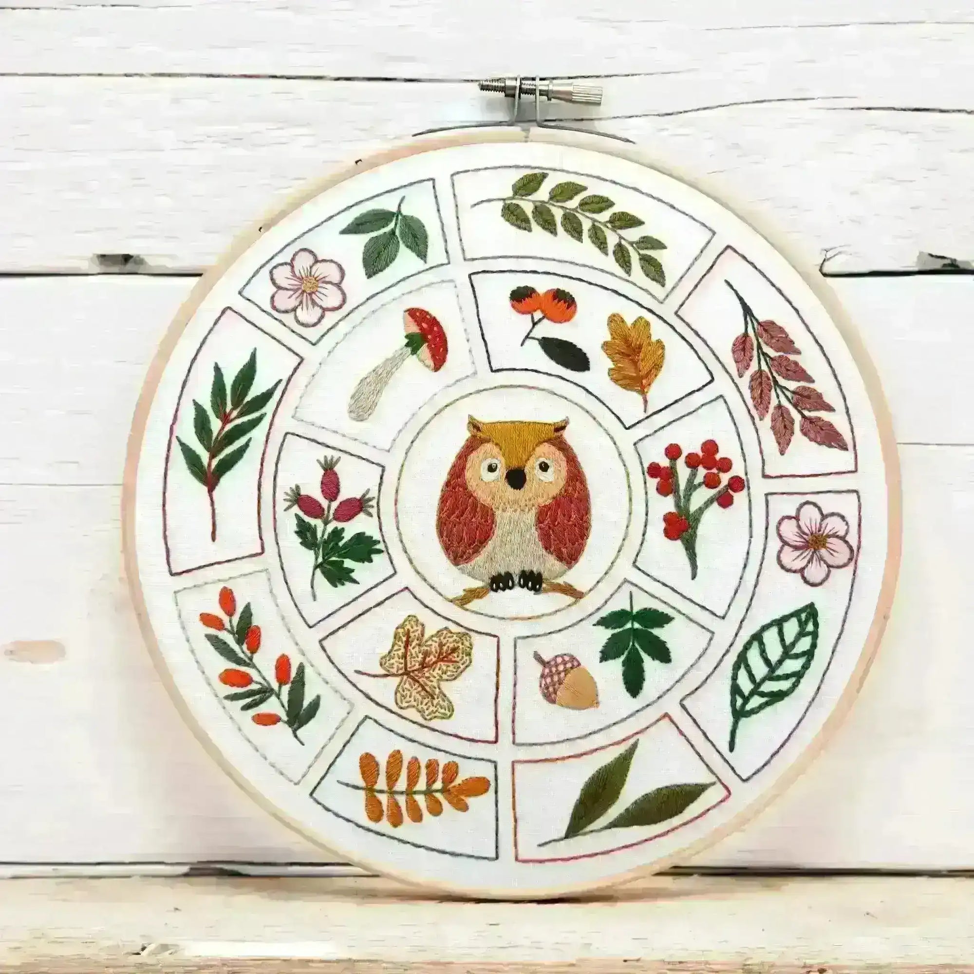 Embroidery hoop with owl design and nature-themed elements on a wooden surface