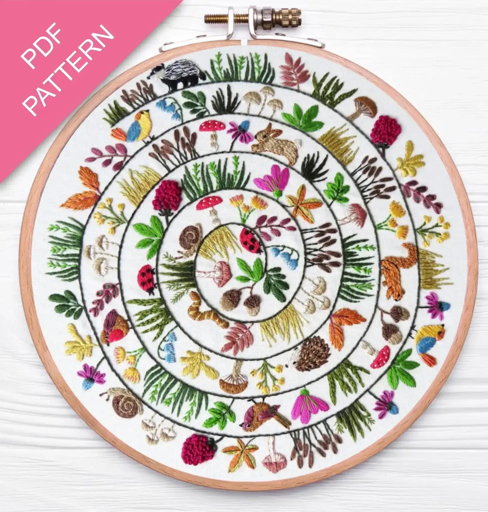 Embroidery hoop with a colorful circular pattern of animals and plants on a white background.