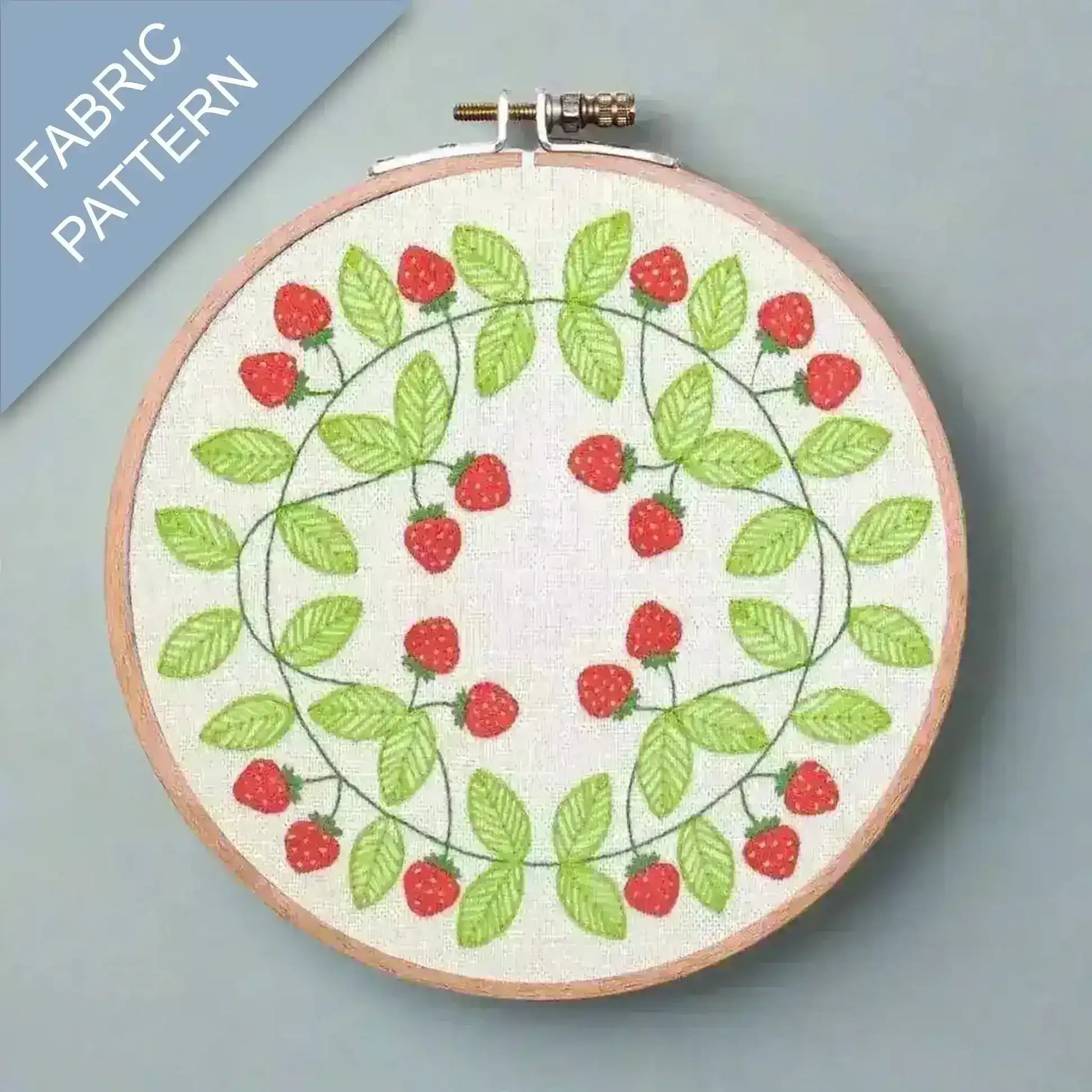 Embroidery hoop with strawberry pattern on fabric, against a gray background.