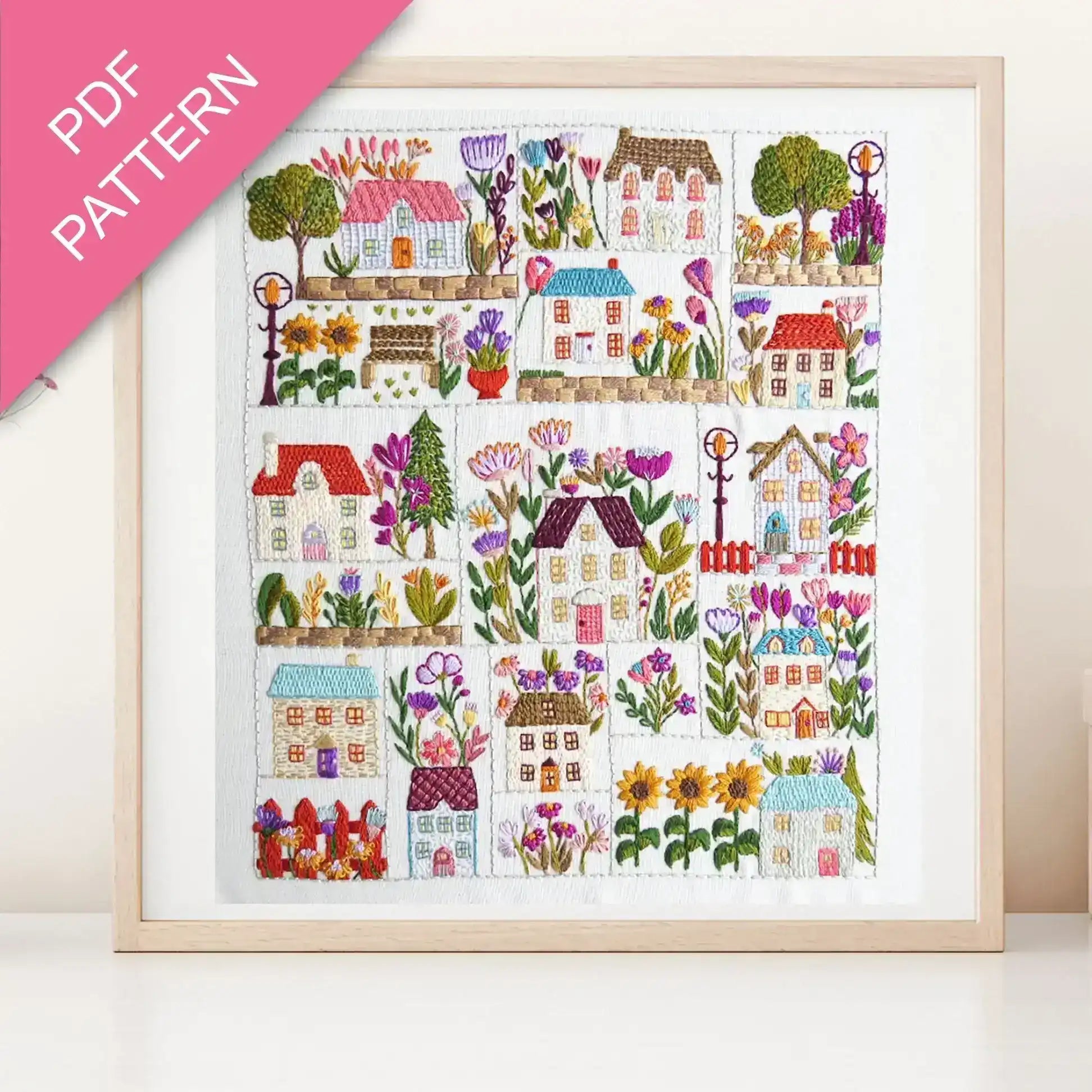 Framed cross-stitch pattern with colorful houses and flowers on a white background
