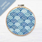 Embroidery hoop with blue and white fabric pattern on a light wooden surface