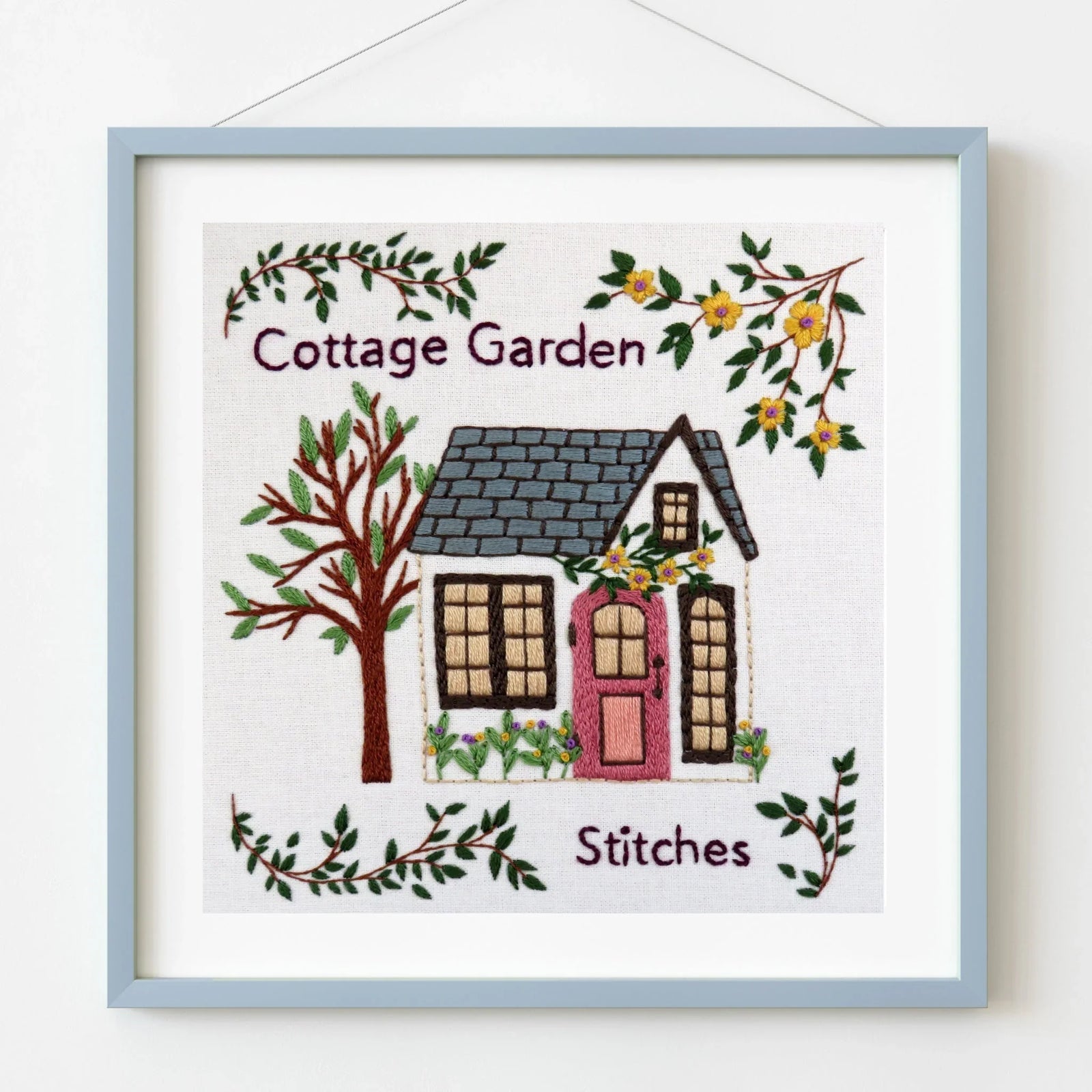 Cottage Garden hand embroidery pattern with pink door, tree, and flowers in light blue frame