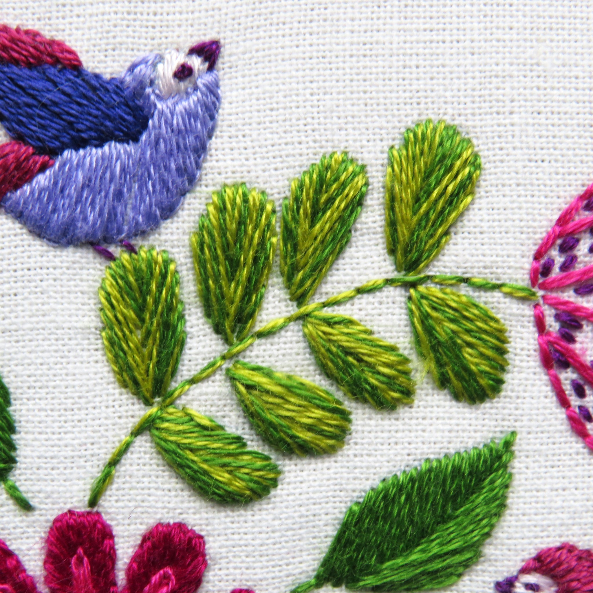 Embroidered design with green leaves and pink flowers on a white background