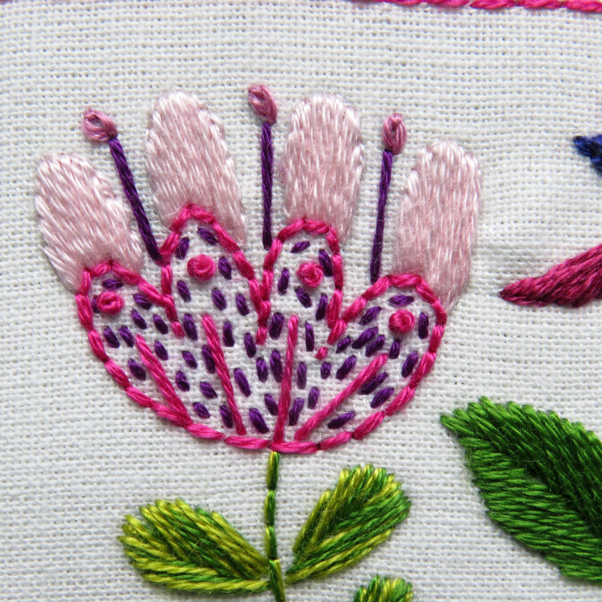 Close-up of embroidered flower with pink and purple petals on a white background