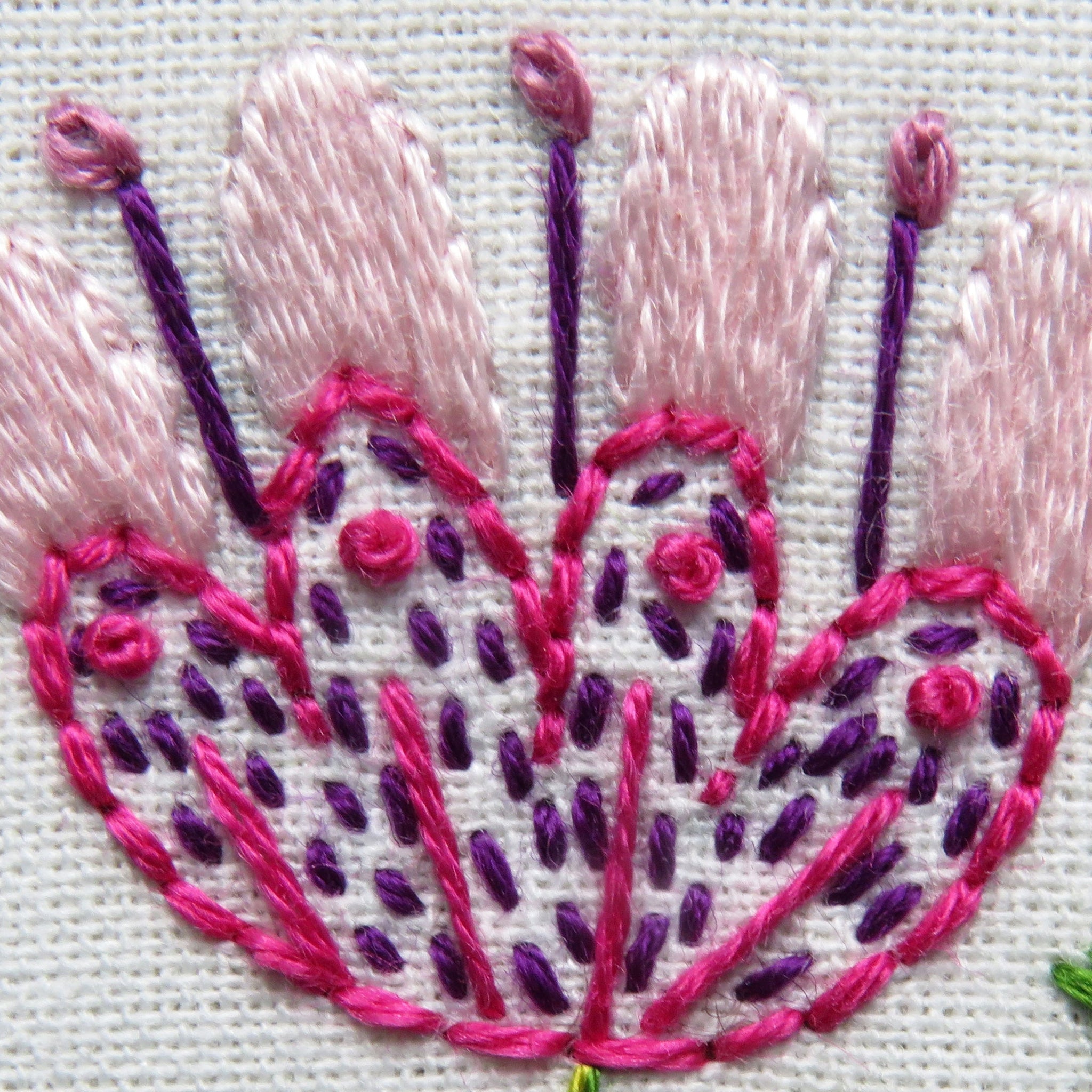 Embroidered flower design with pink and purple threads on a white background
