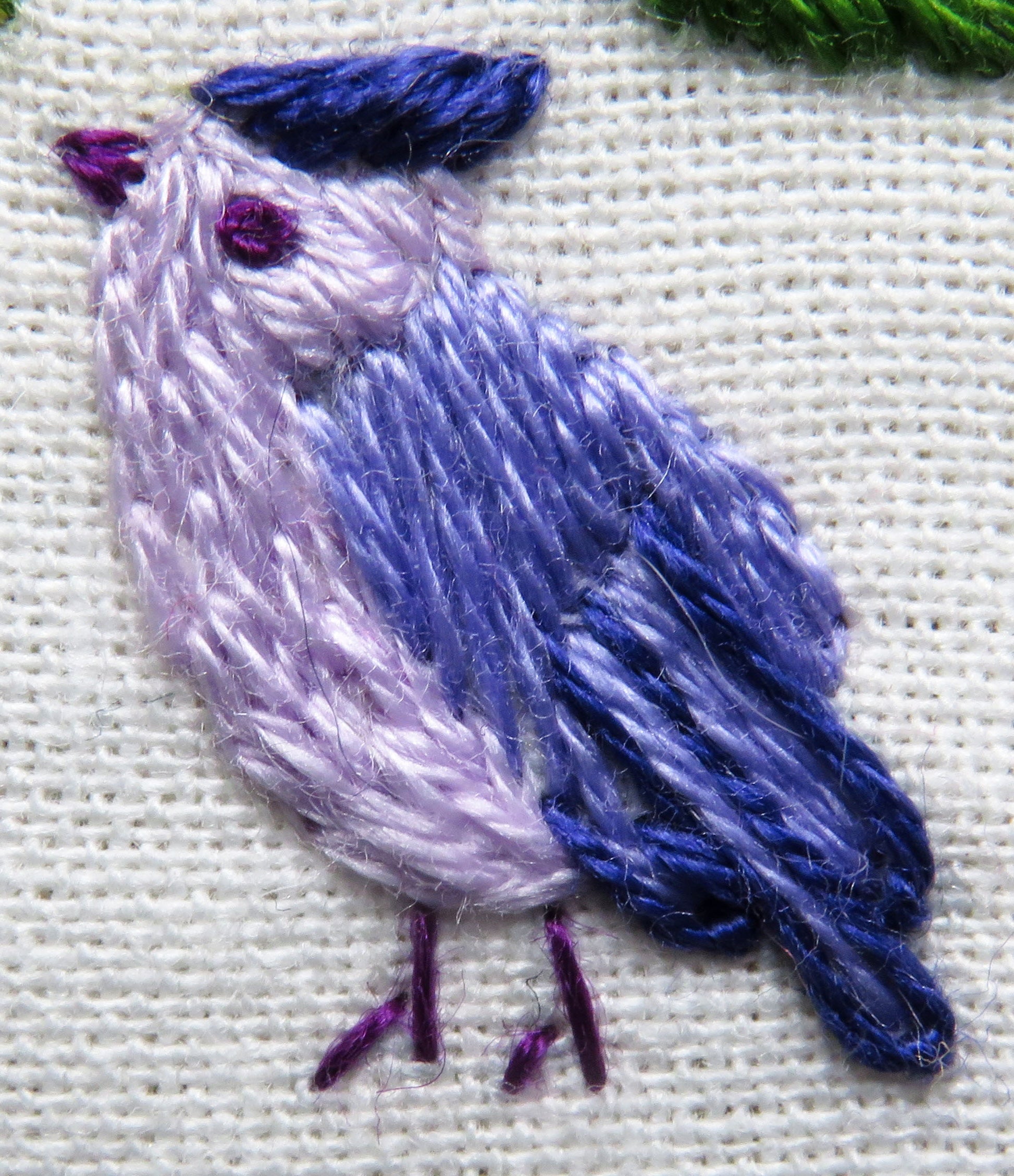 Embroidered bird design on fabric with purple and blue colors.