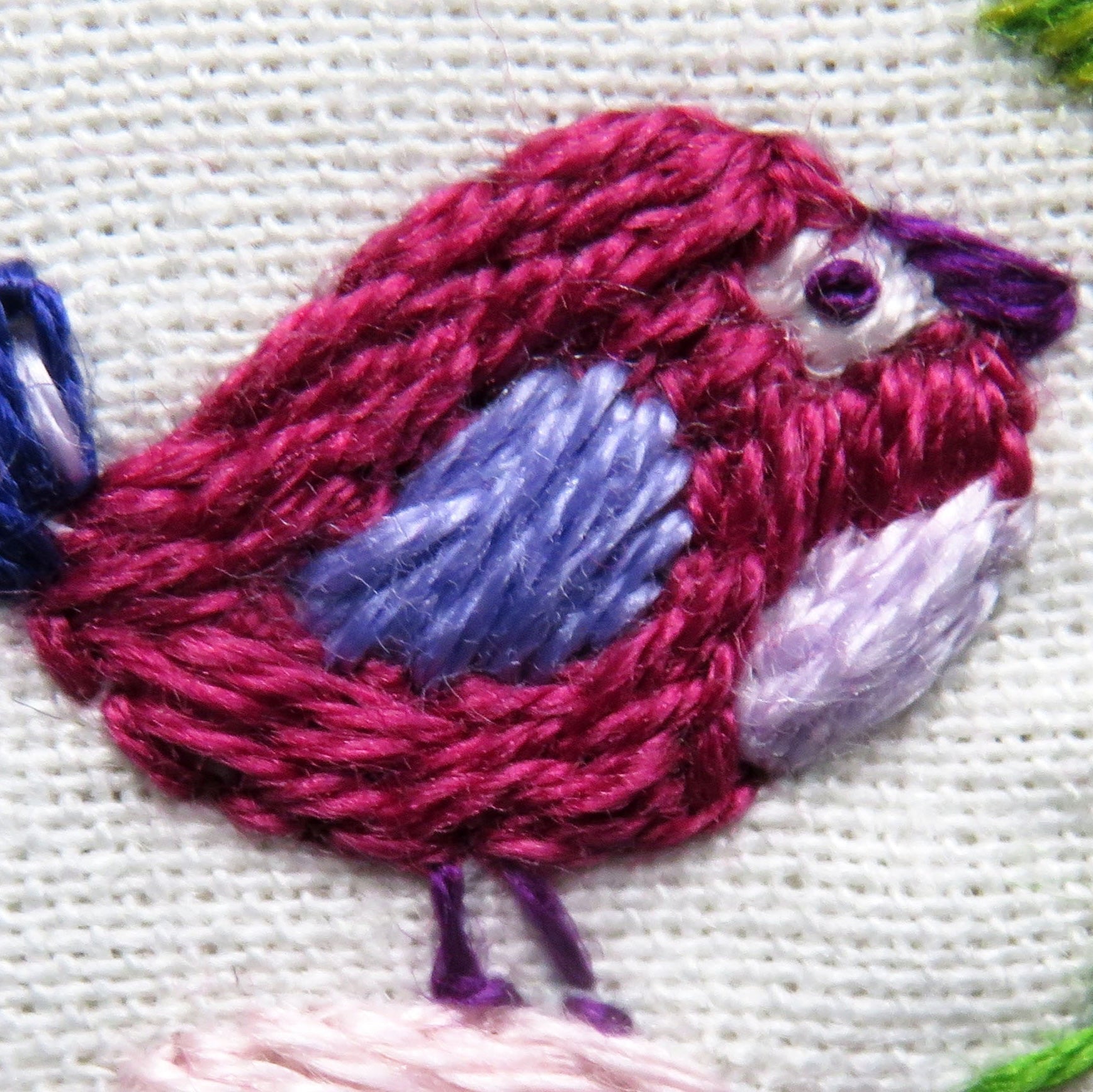 Embroidered pink bird on a white fabric background