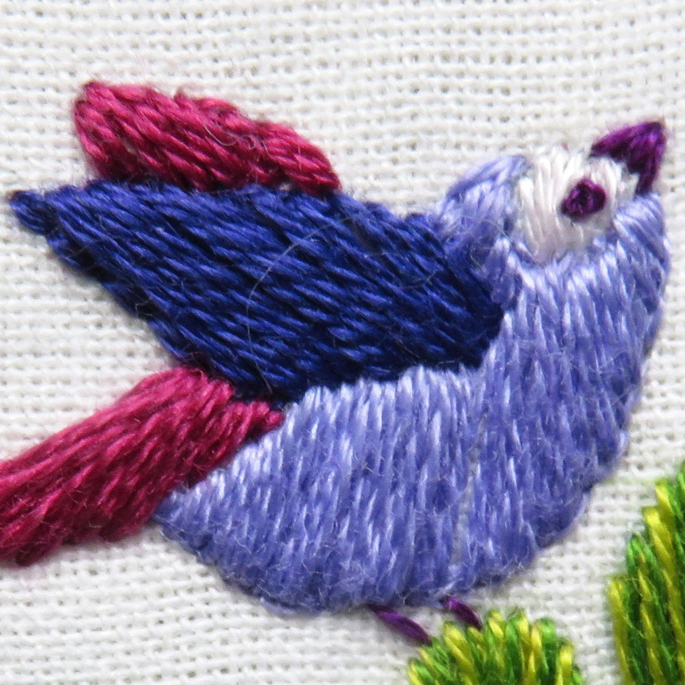 Embroidered bird design on fabric with pink and blue colors.