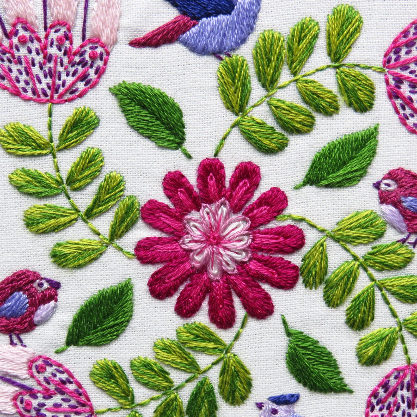 Close-up of embroidered floral design with pink flowers and green leaves on a white background.