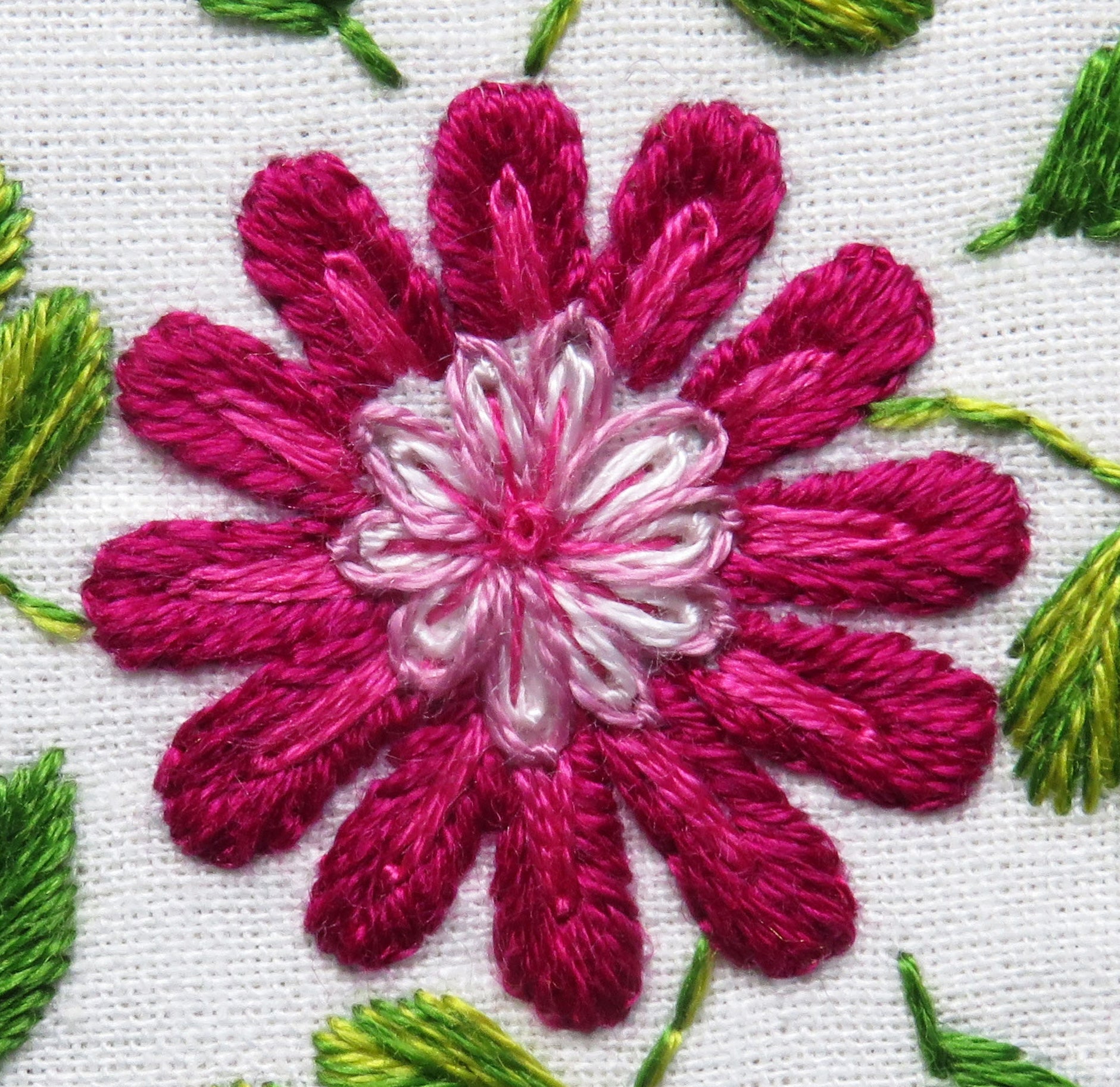 Embroidered flower design with pink petals and green leaves on a white background