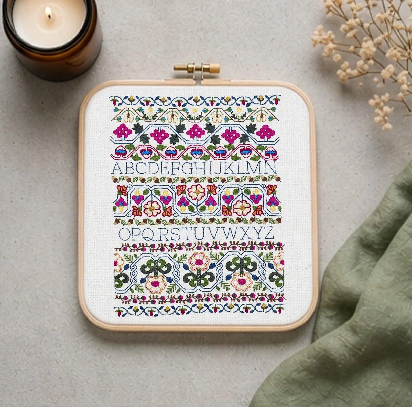 Colorful hand embroidery pattern with floral designs and alphabet letters in wooden hoop