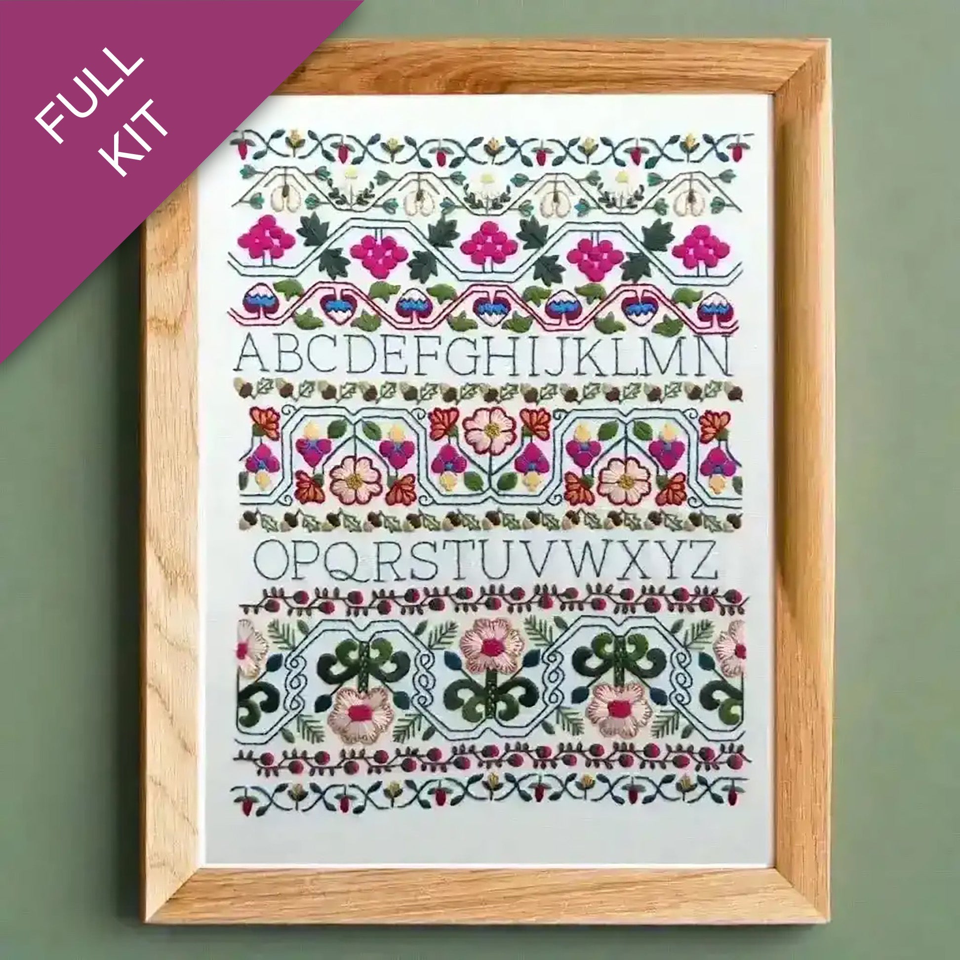 Embroidery kit with floral alphabet design in a wooden frame on a green background