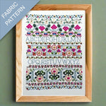 Framed fabric pattern with embroidered letters and designs on a green background