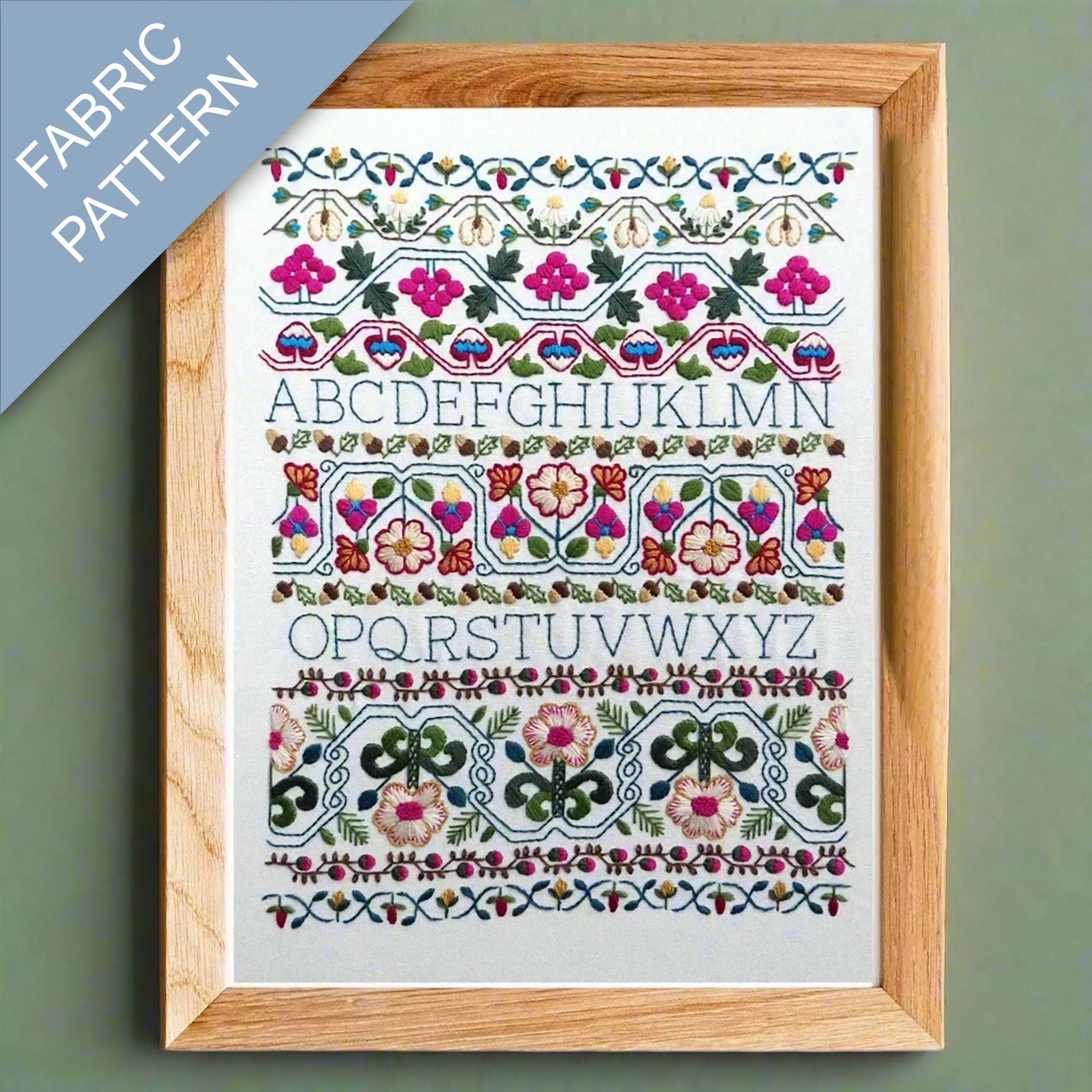 Framed fabric pattern with embroidered letters and designs on a green background