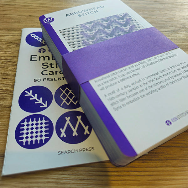 Two books on embroidery stitches on a wooden surface