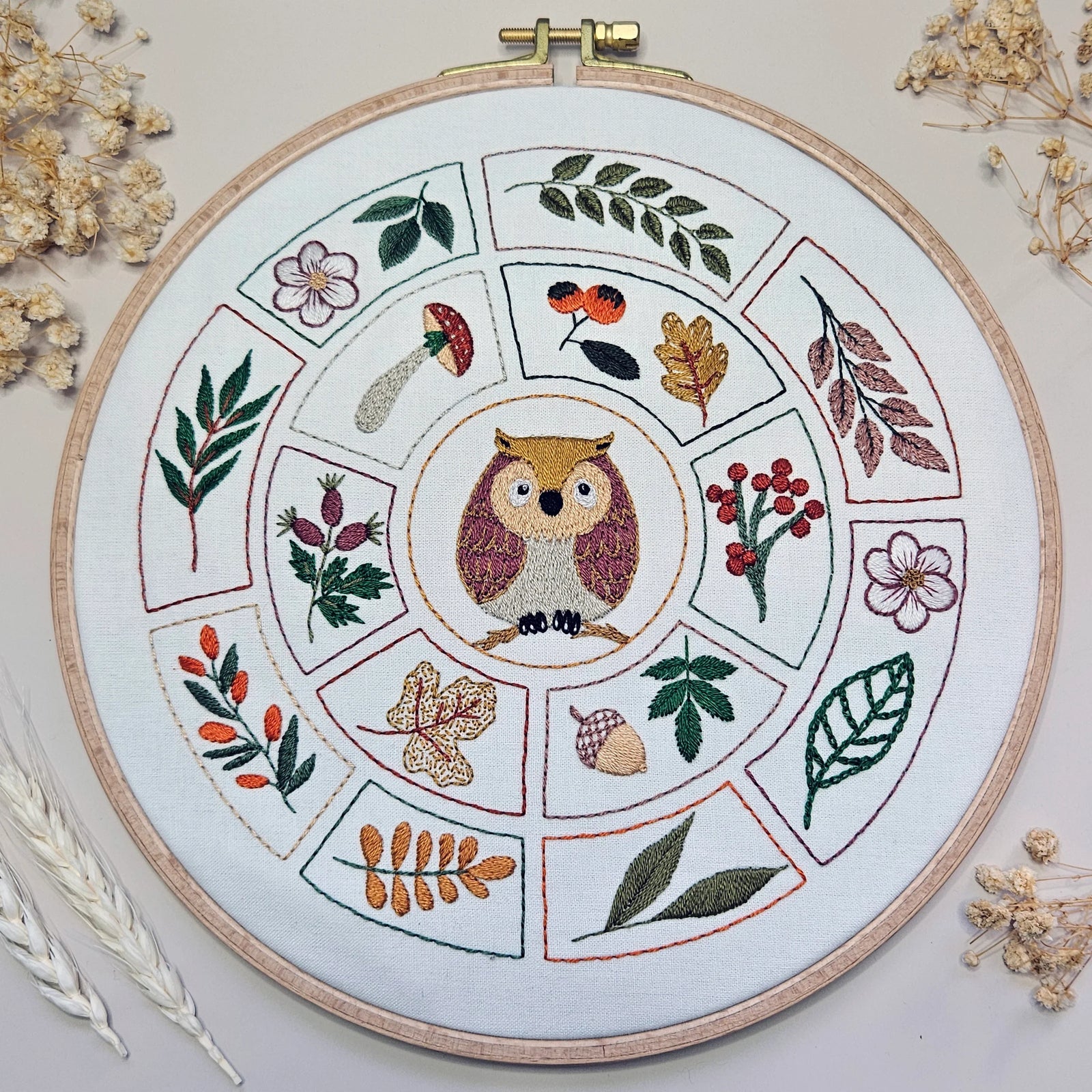 Embroidery hoop with owl design surrounded by leaves and flowers on a light background