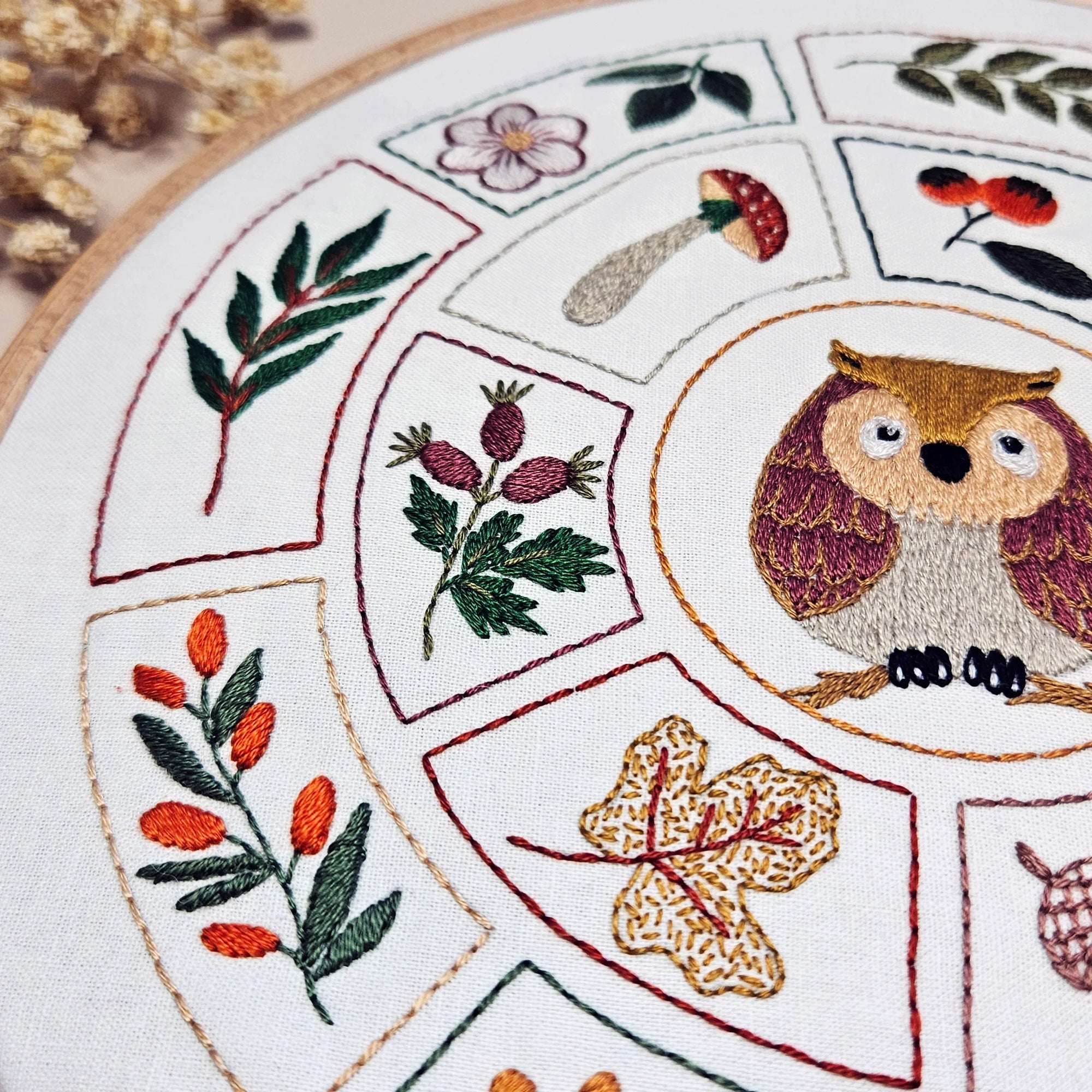 Embroidery hoop with owl and nature-themed designs on a white background
