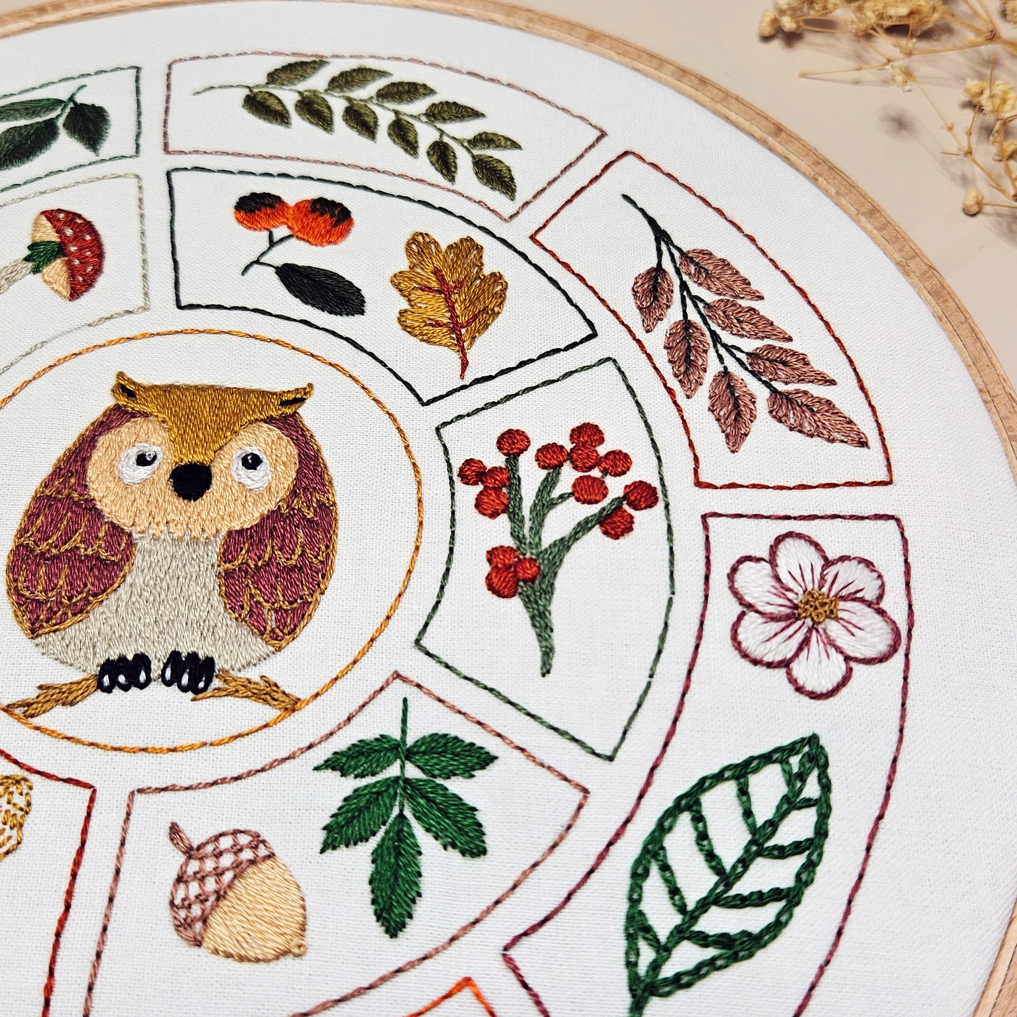 Embroidered design with owl, leaves, and berries on a circular pattern.