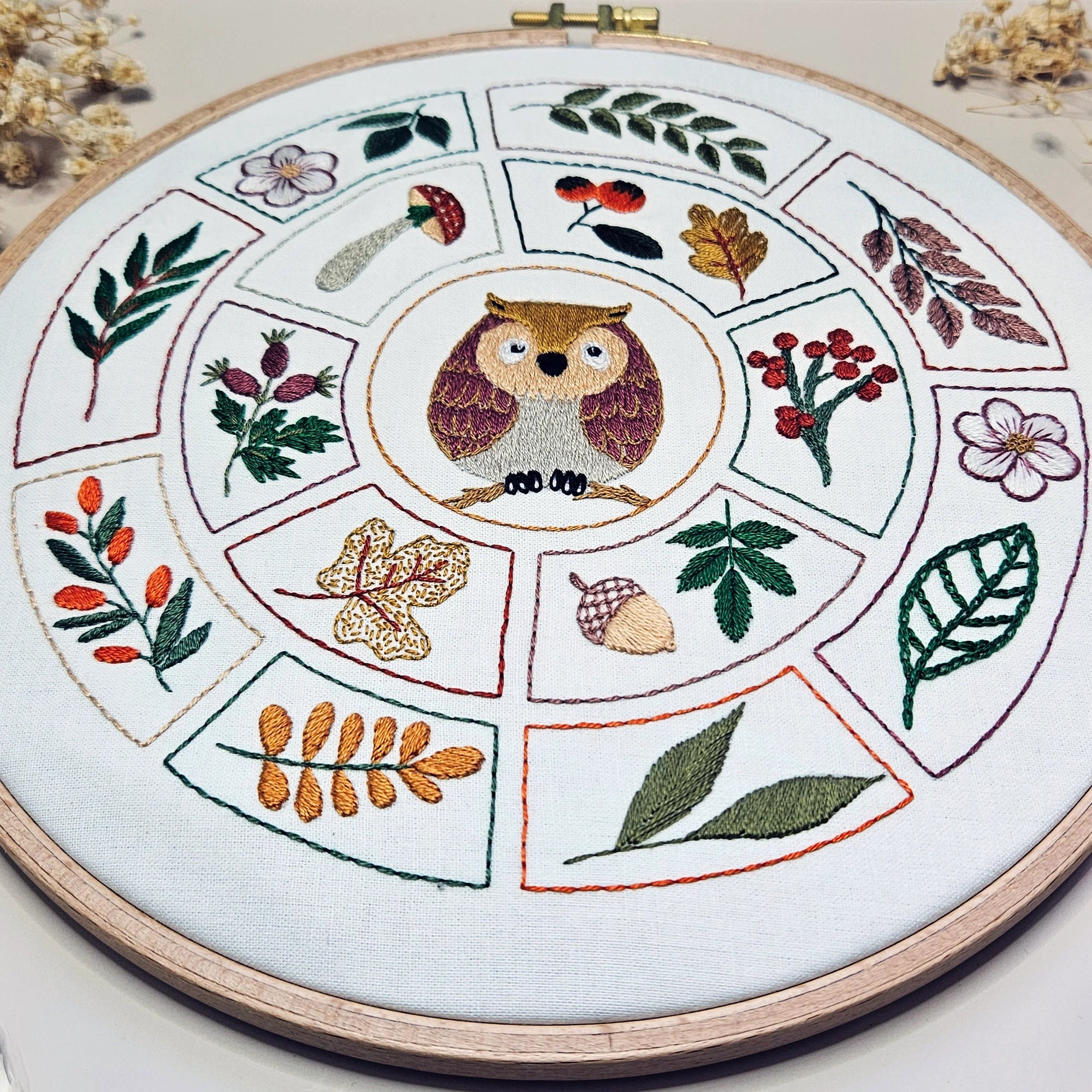 Embroidery hoop with owl design and nature-themed elements on a white background