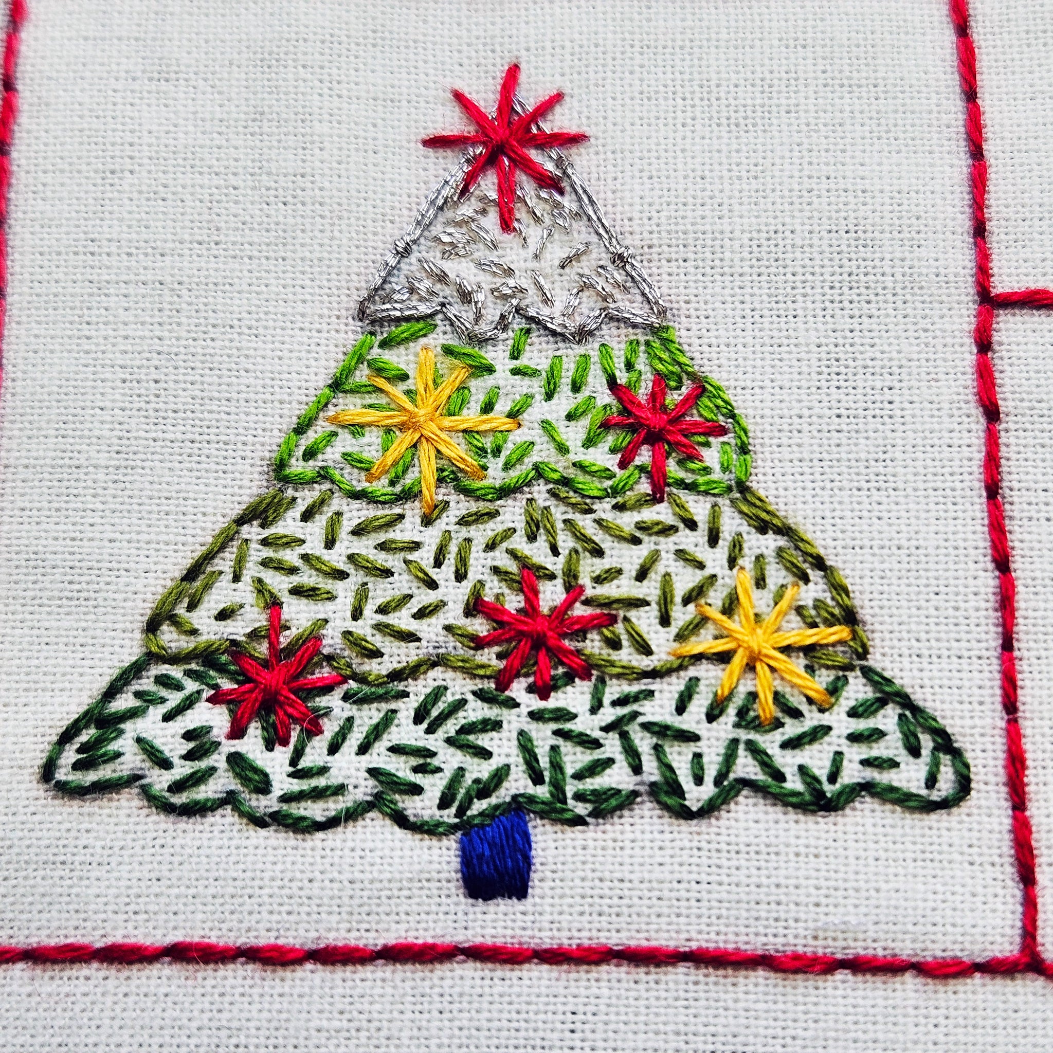 Embroidered Christmas tree design on fabric with red, green, and yellow colors.