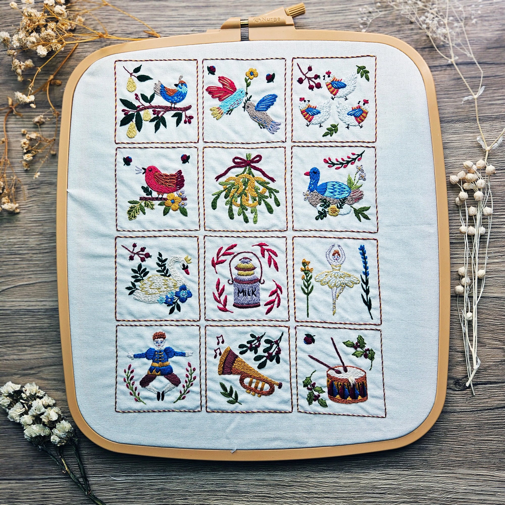 Embroidered patchwork design on a wooden surface with dried flowers.