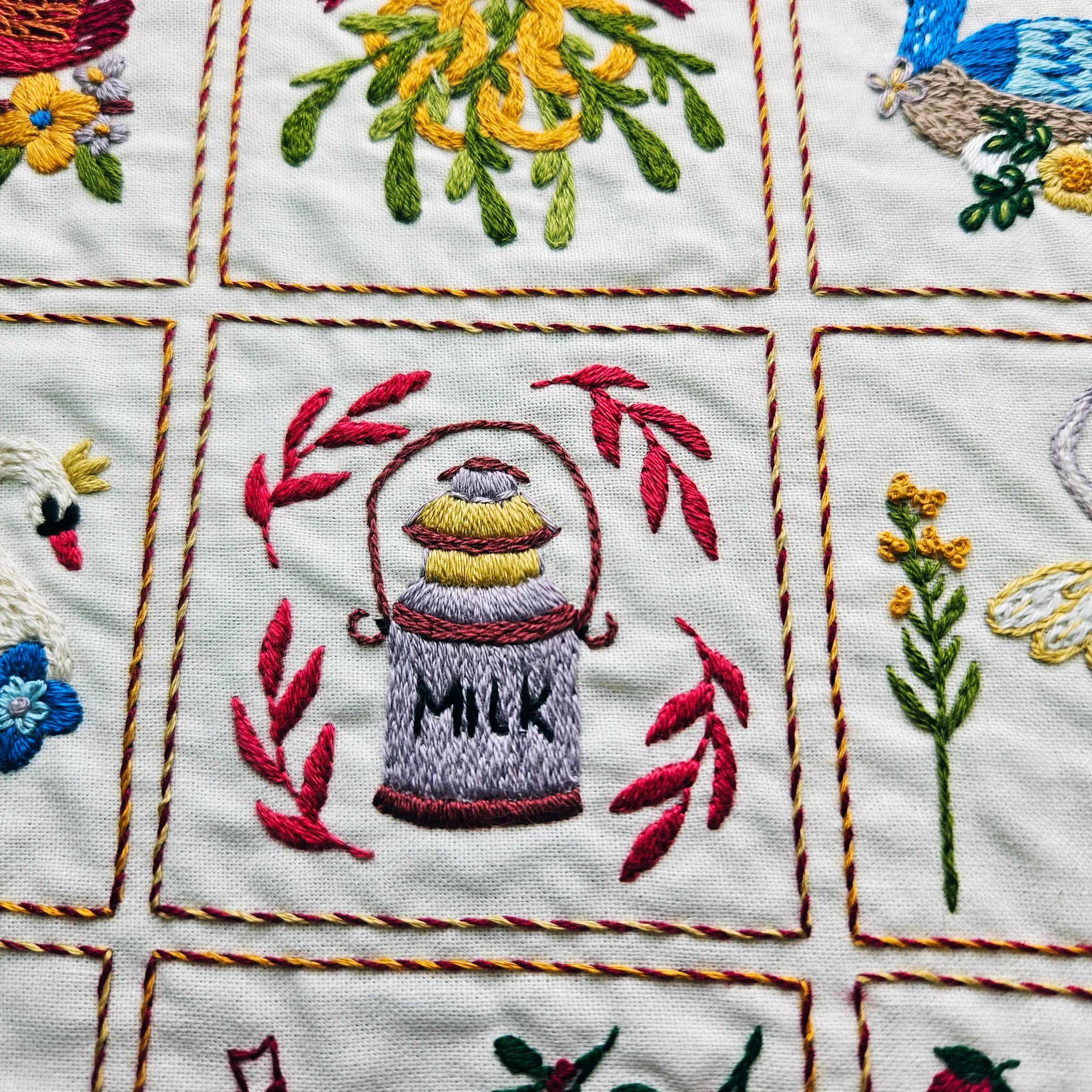 Embroidered design of a milk bottle with leaves on a quilted fabric background.