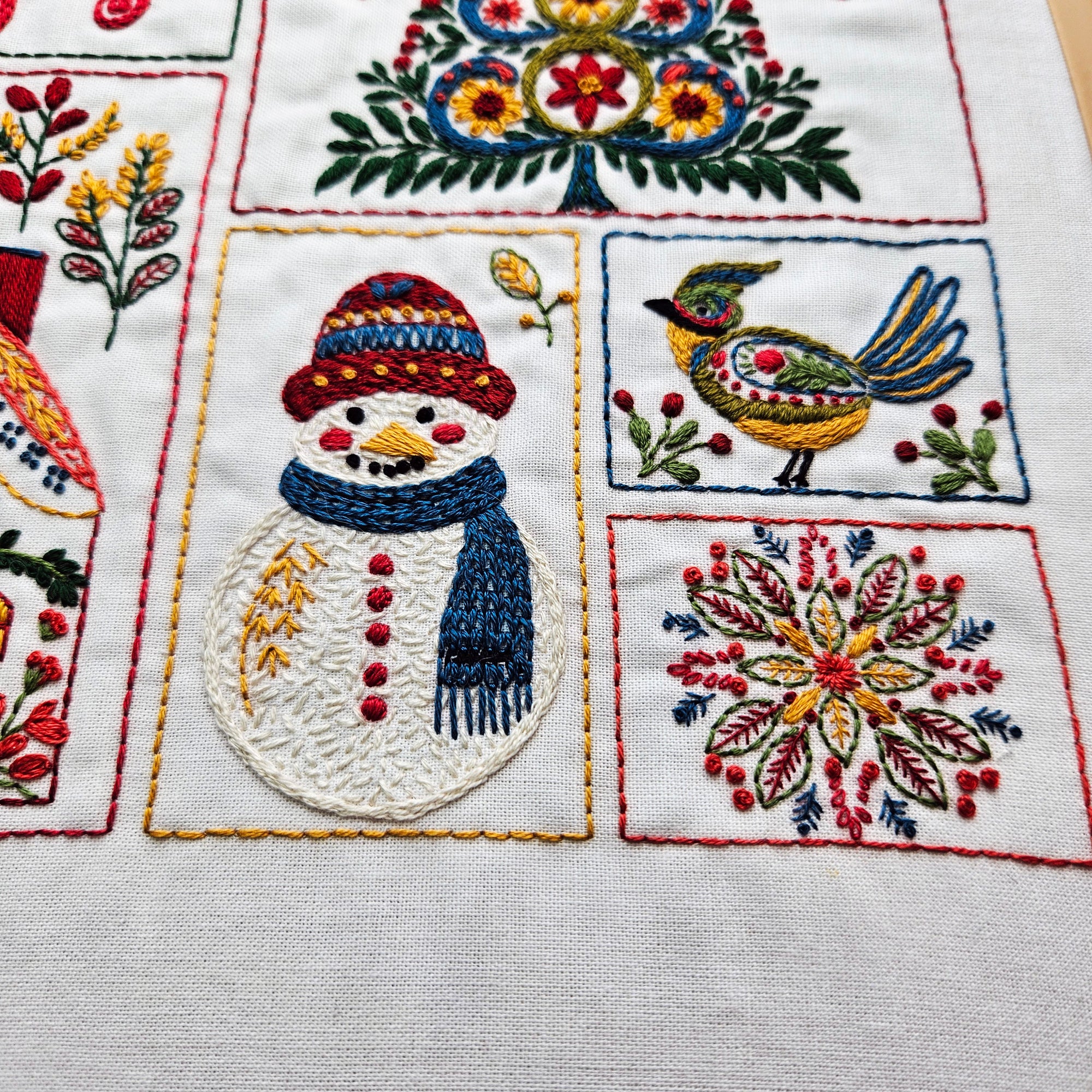 Embroidered fabric with a snowman, bird, and floral patterns on a white background.