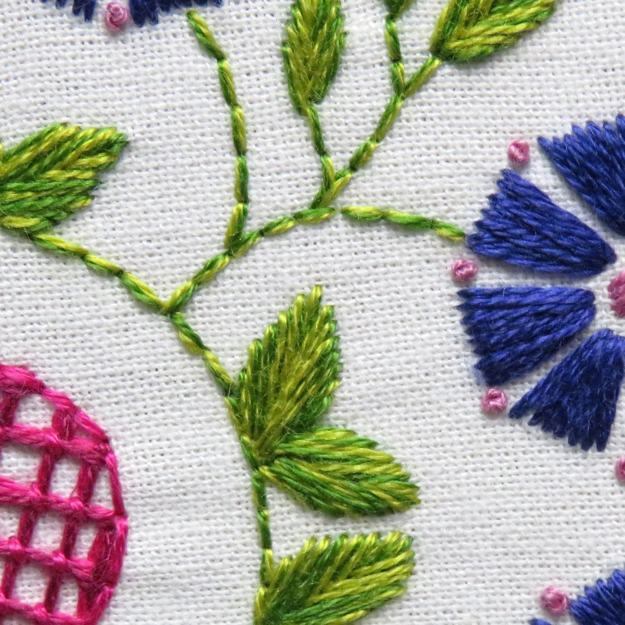 Close-up of embroidered floral design with blue, green, and pink colors on a white background.