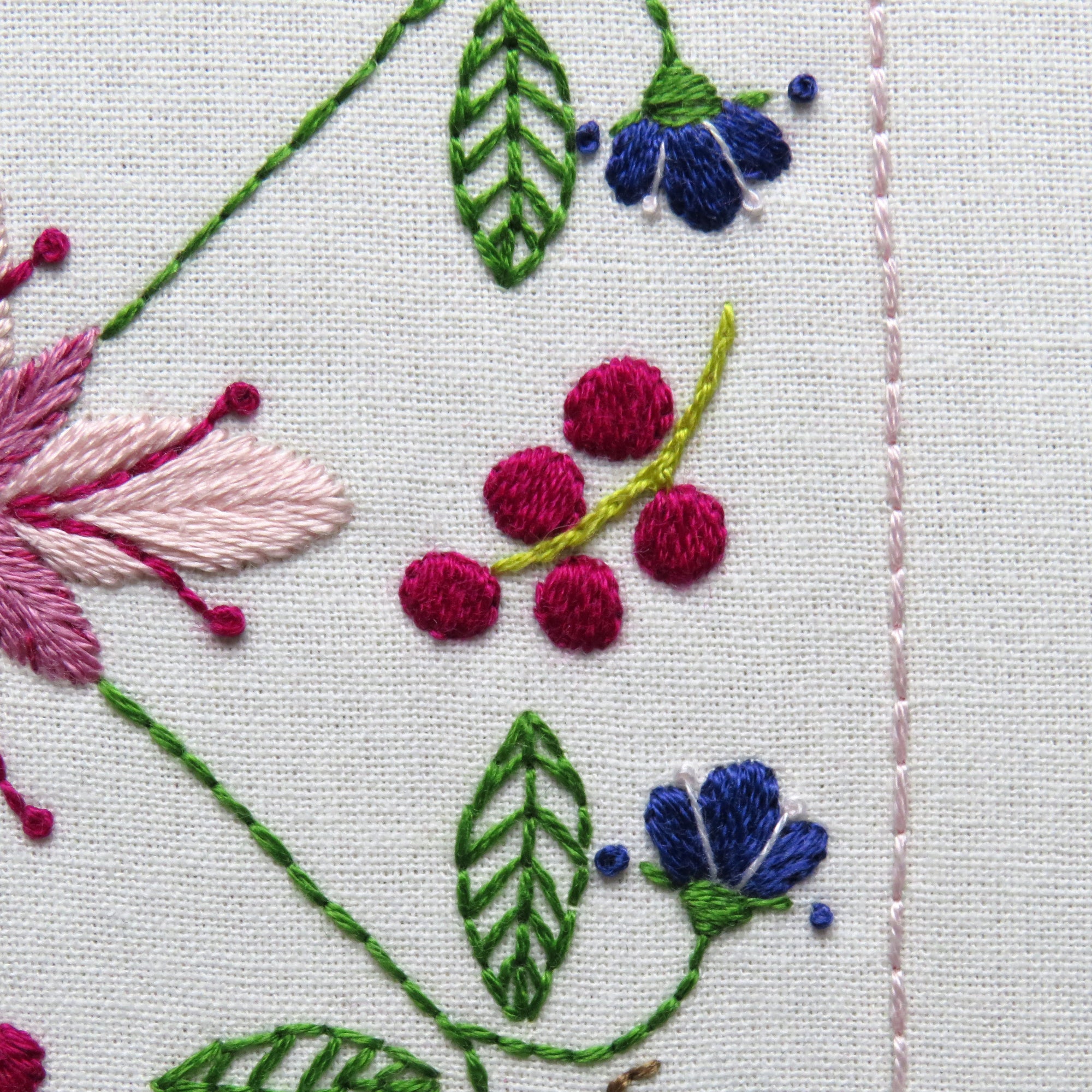 Close-up of embroidered floral design with pink, purple, and green colors on a white background.