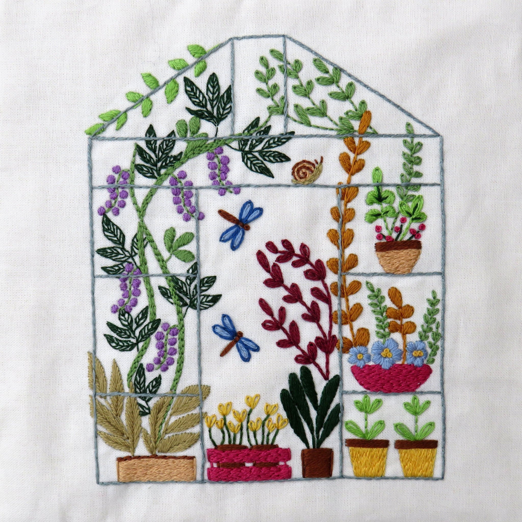 Embroidered design of a greenhouse with plants on a white fabric background
