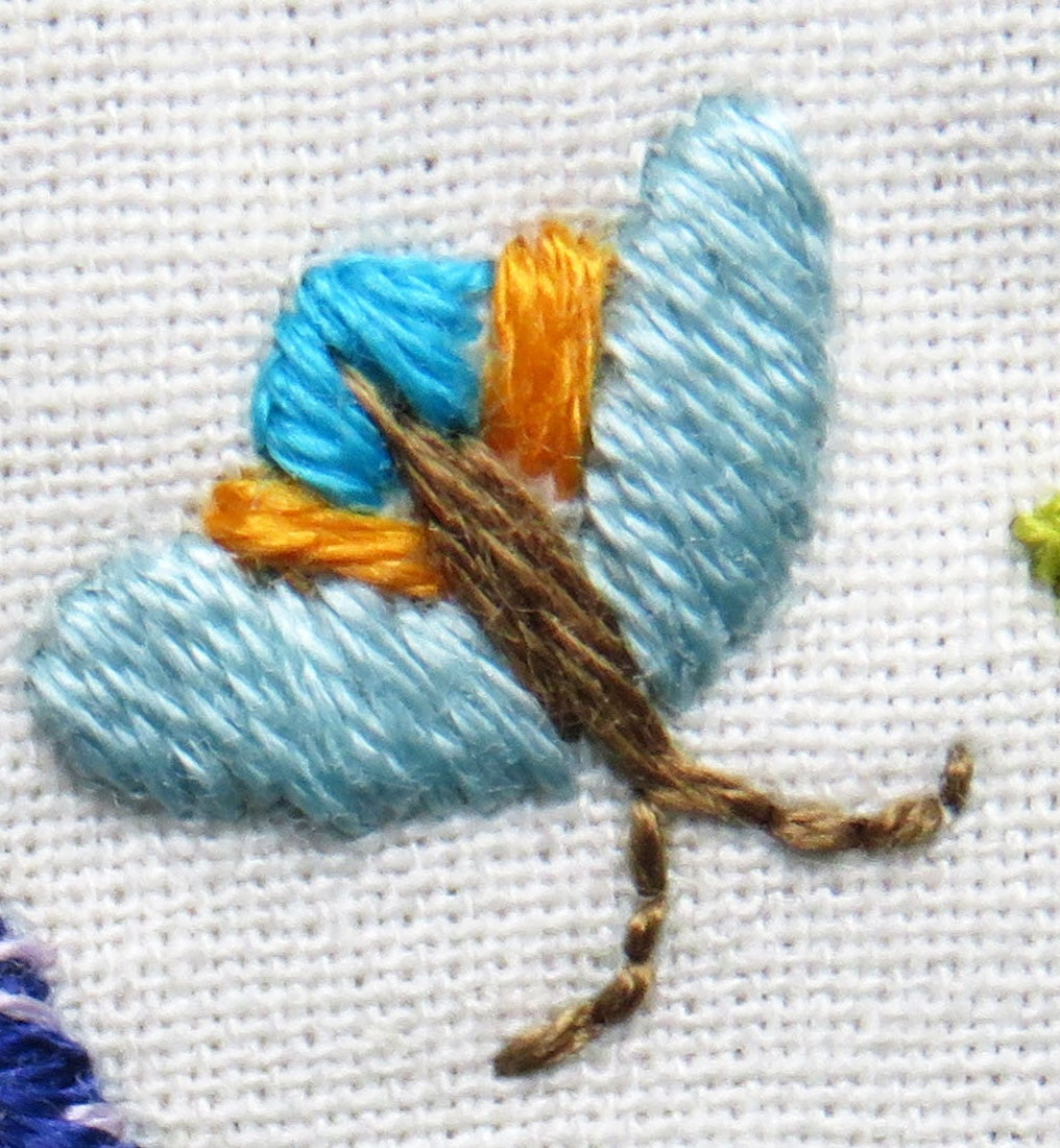 Close-up of embroidered butterfly with blue wings and brown body on white fabric