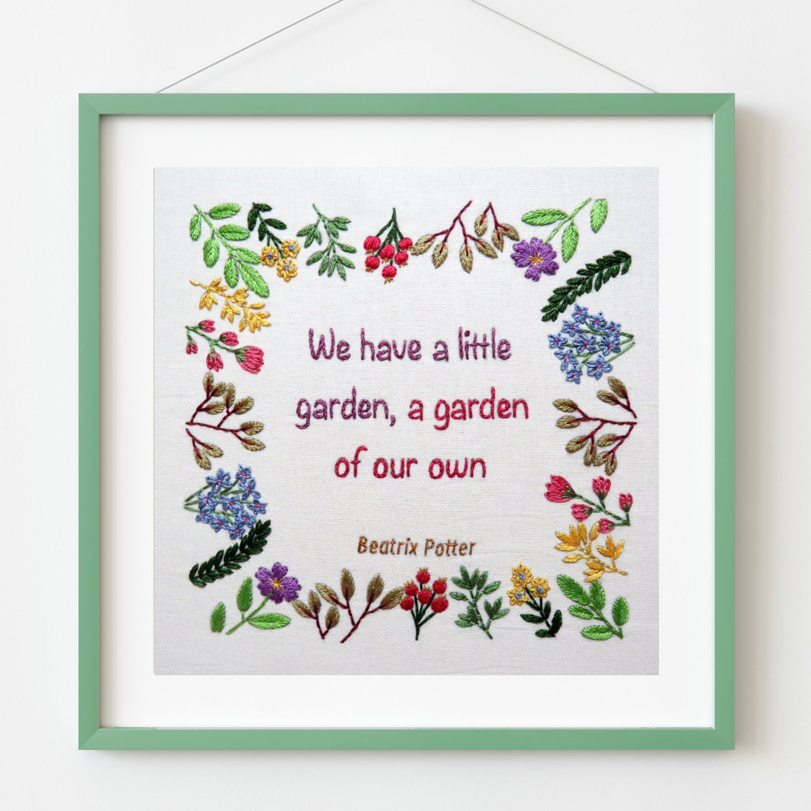 Framed embroidery with floral designs and text on a white background