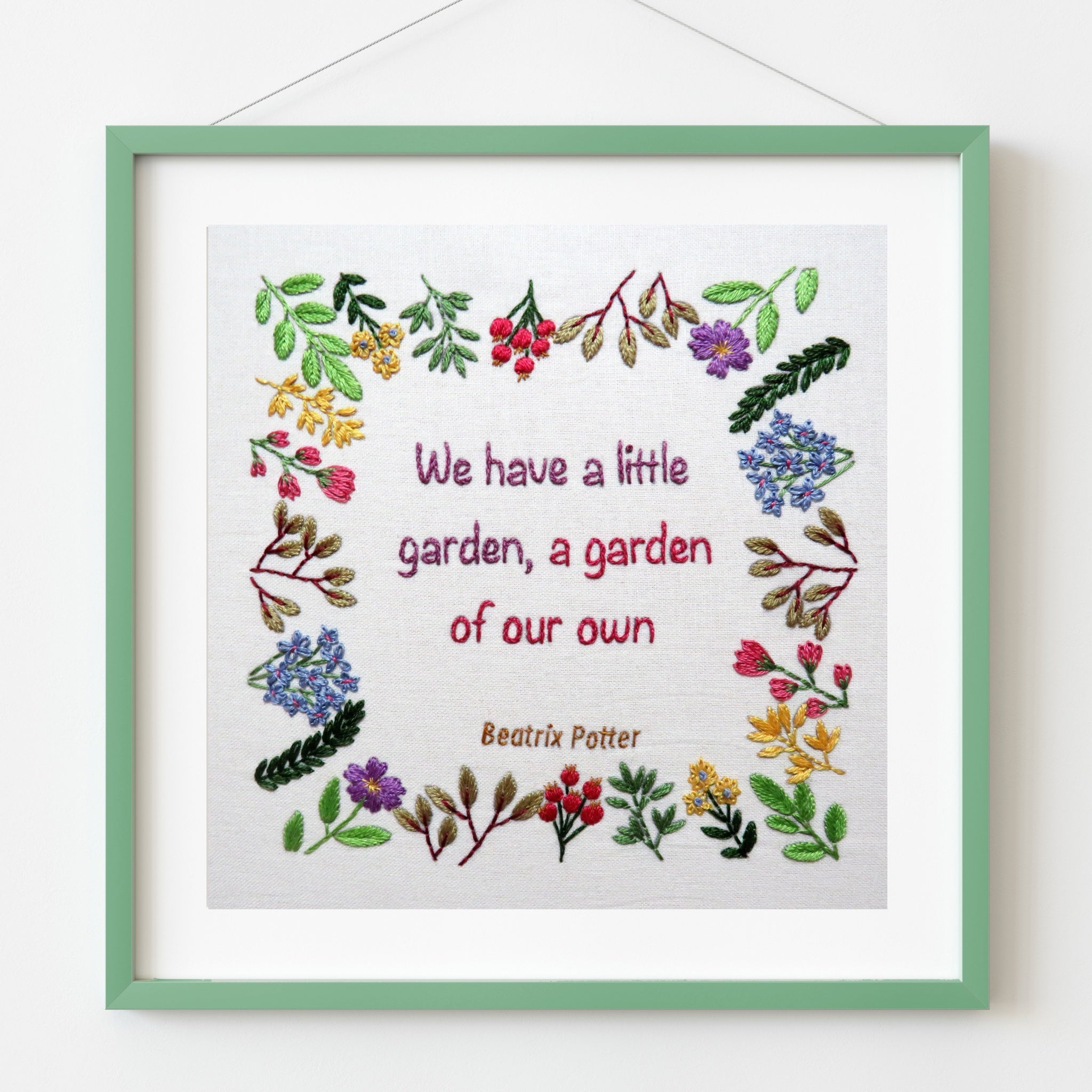 Framed embroidery with floral designs and text on a white background