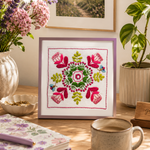 Decorative table setting with a framed floral embroidery, mug, notebook, and candles.